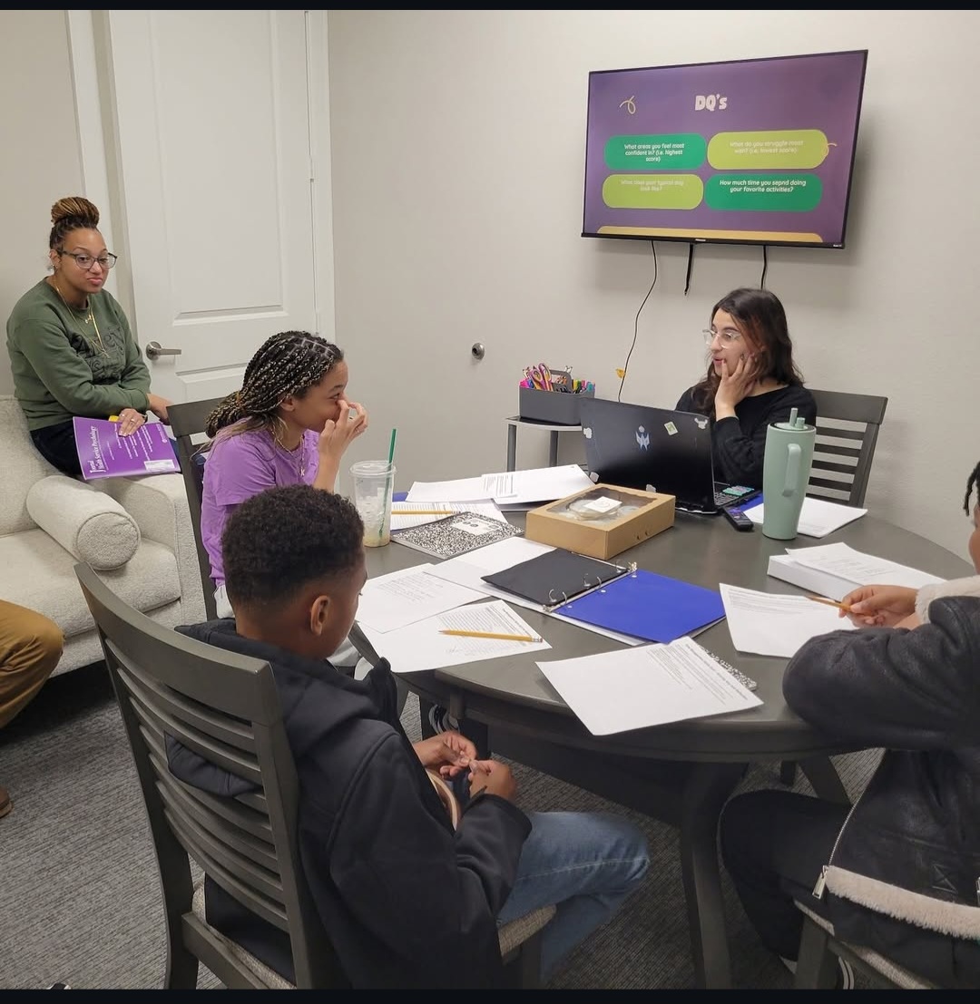 Group of five people in a meeting room with a TV screen, papers, and laptops on the table.