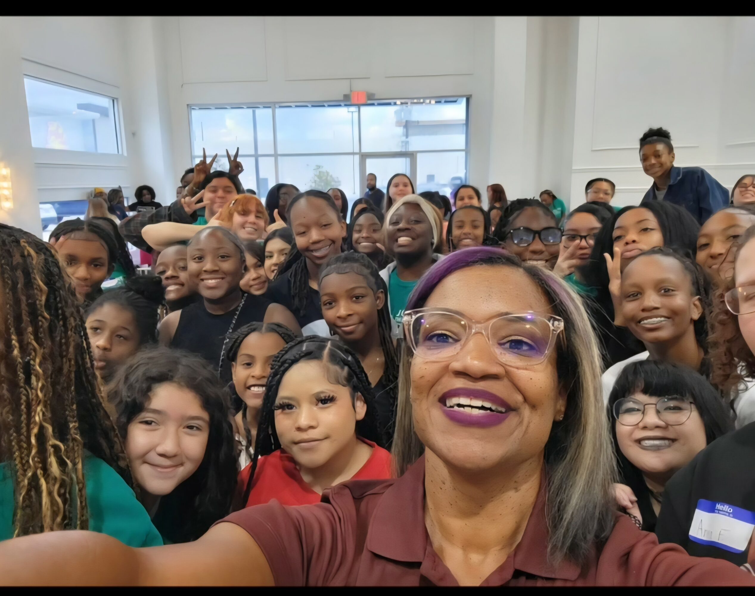 Group of children and a woman taking a selfie indoors, smiling and looking at the camera.