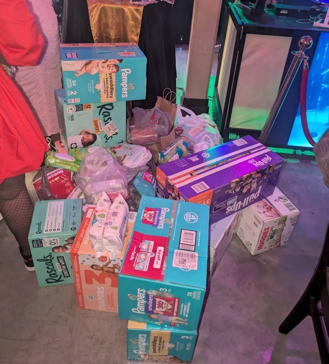 Various boxes and packages of snacks and drinks on the floor, with people standing nearby in a room with colorful lighting.