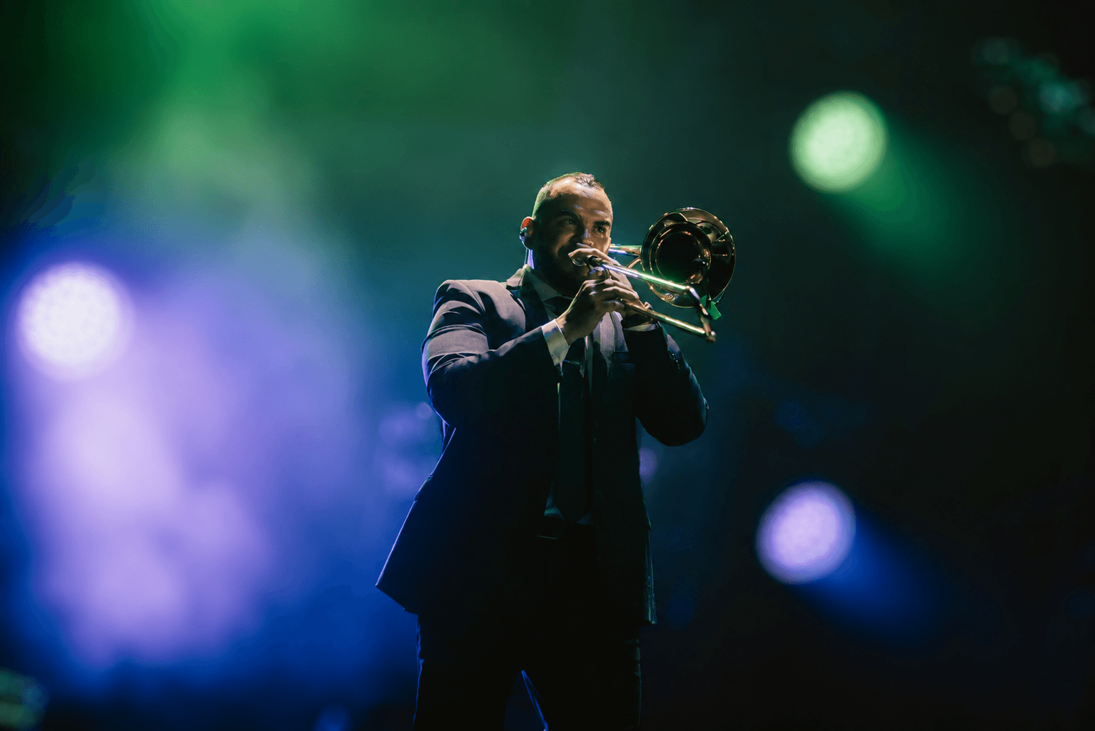 Person playing trumpet on stage with colorful lights in background.