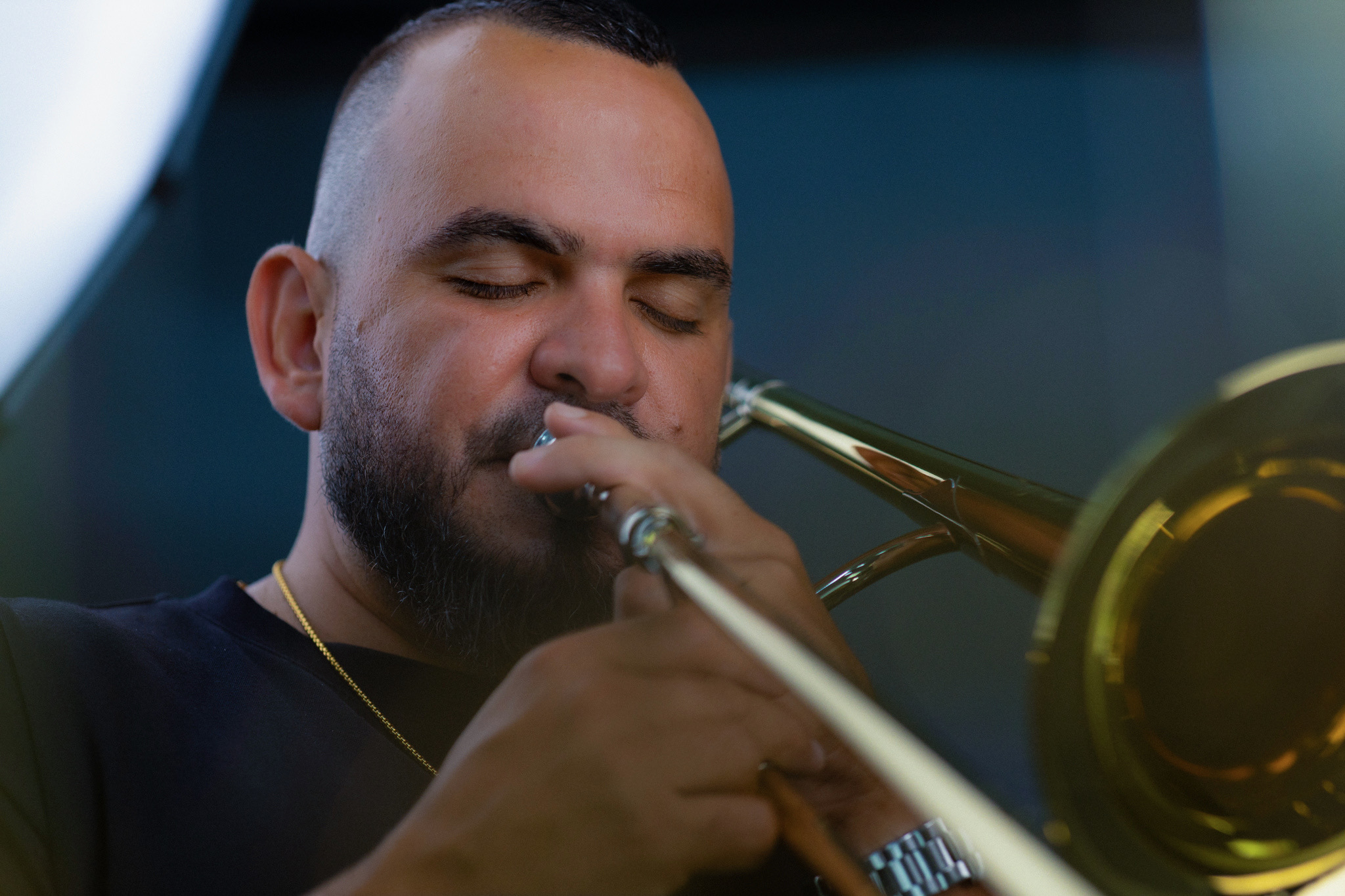 Person playing trumpet with eyes closed, focused on music, in a dark indoor setting.