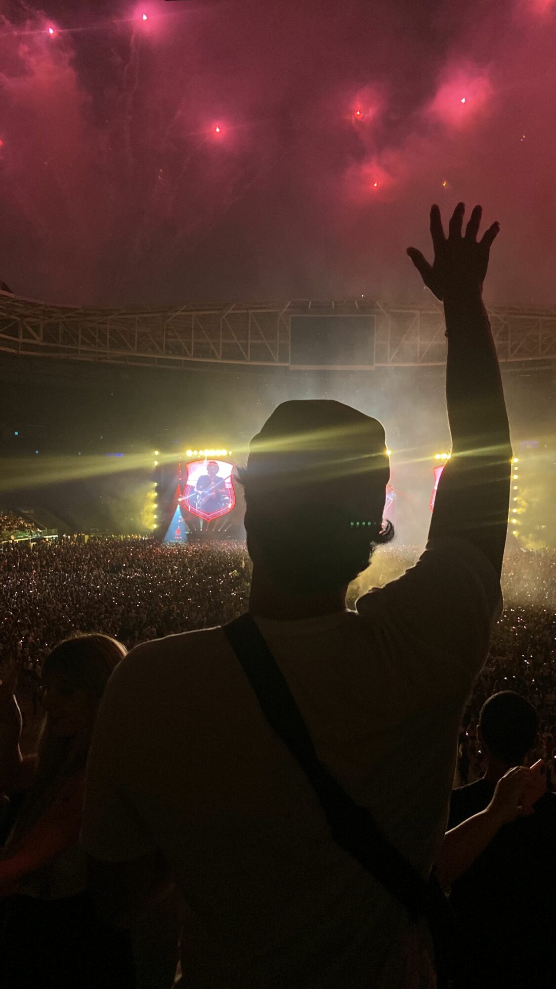 Person waving at a stadium with a colorful sky and bright lights, silhouette visible against the background.