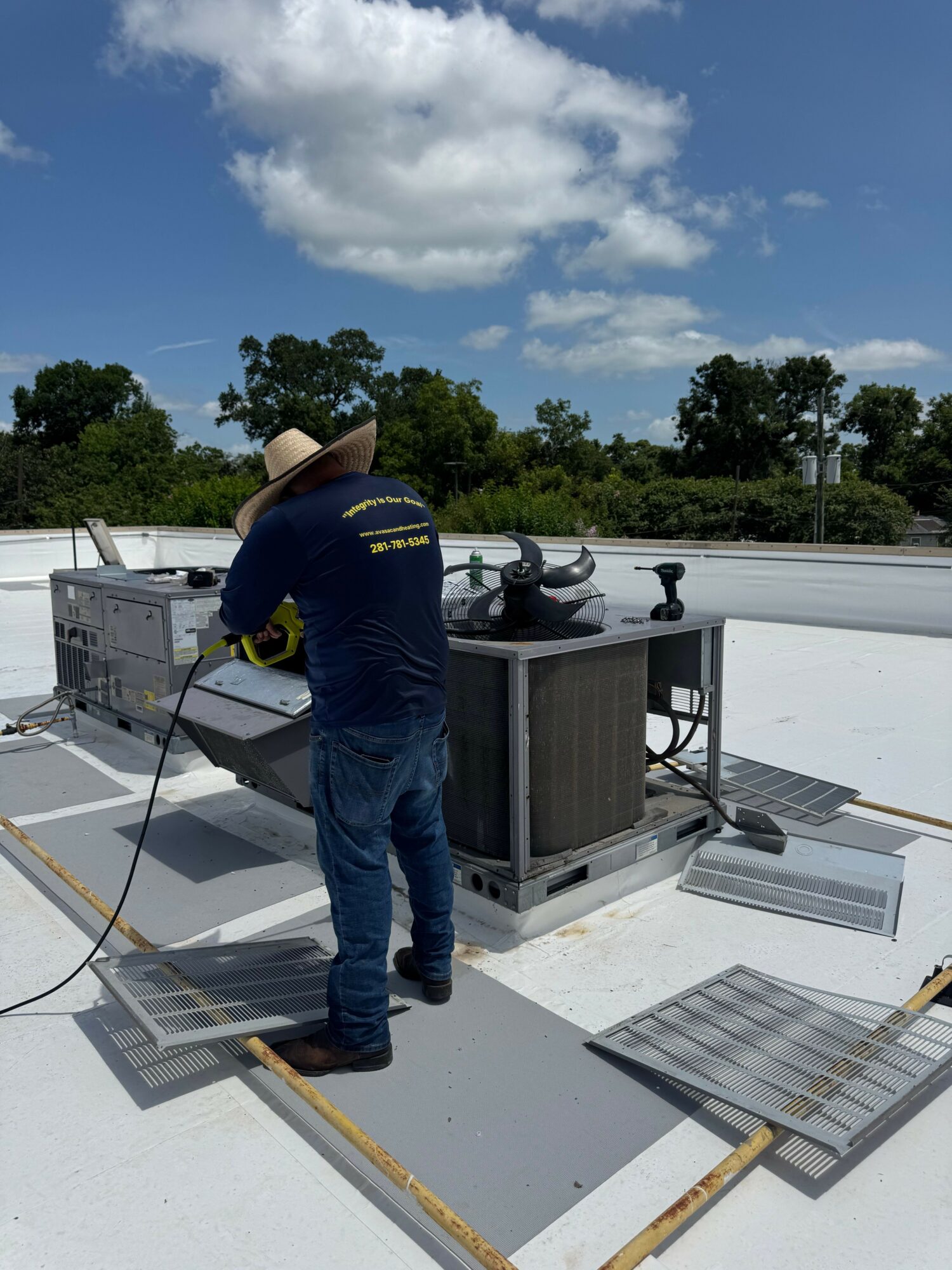 Person wearing a hat and jeans working on a rooftop with equipment and a cloudy sky.
