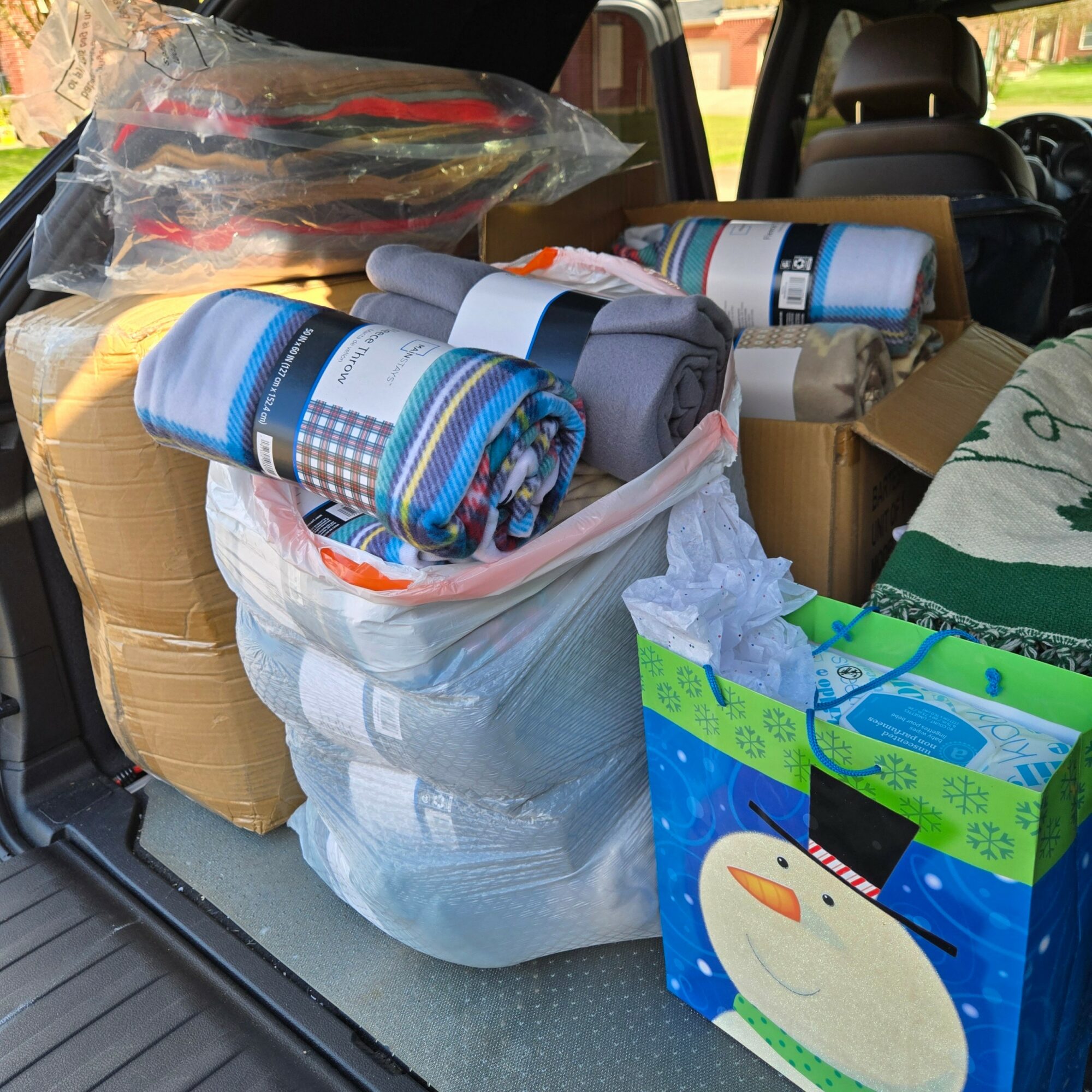 Car trunk filled with rolled-up blankets, boxes, and a gift bag with a duck design, packed for moving or storage.