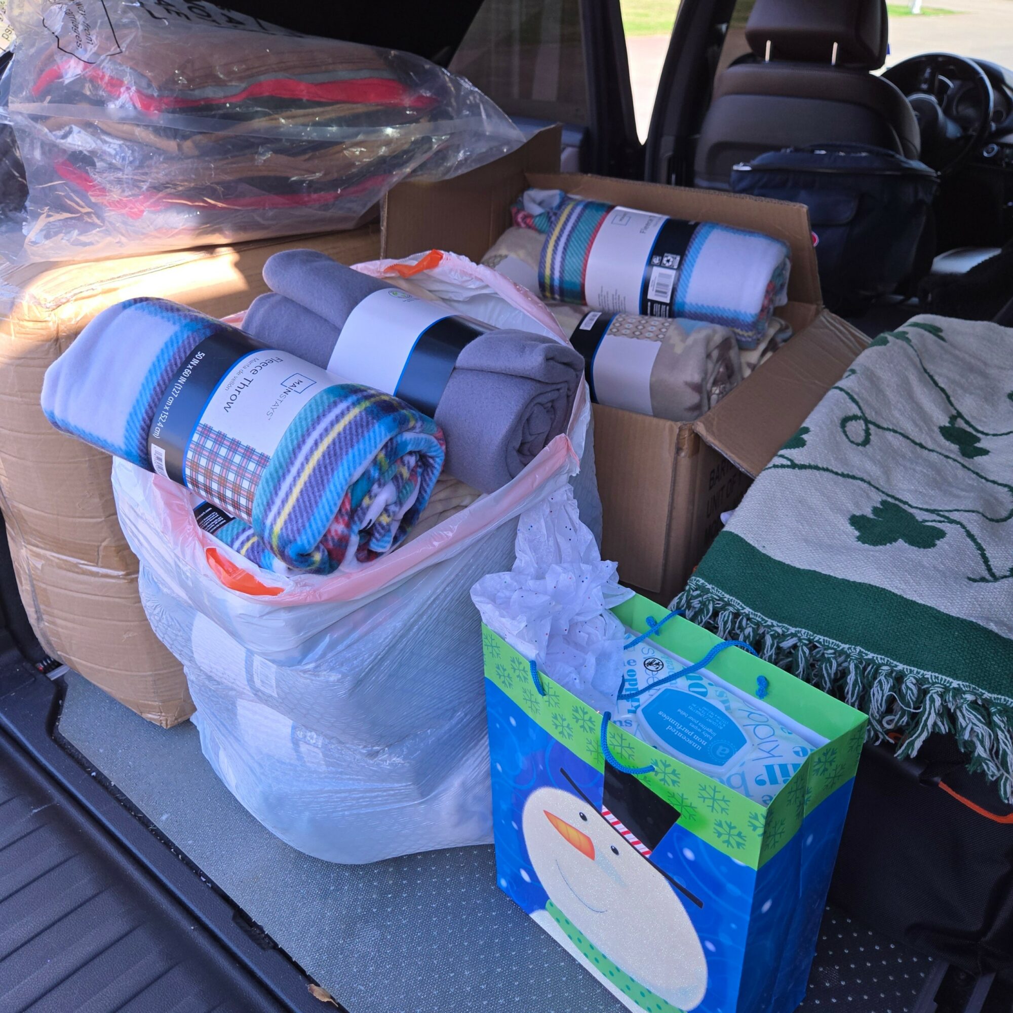Car trunk filled with rolled-up blankets, a box, and a bag, with seats and a blanket visible inside the vehicle.