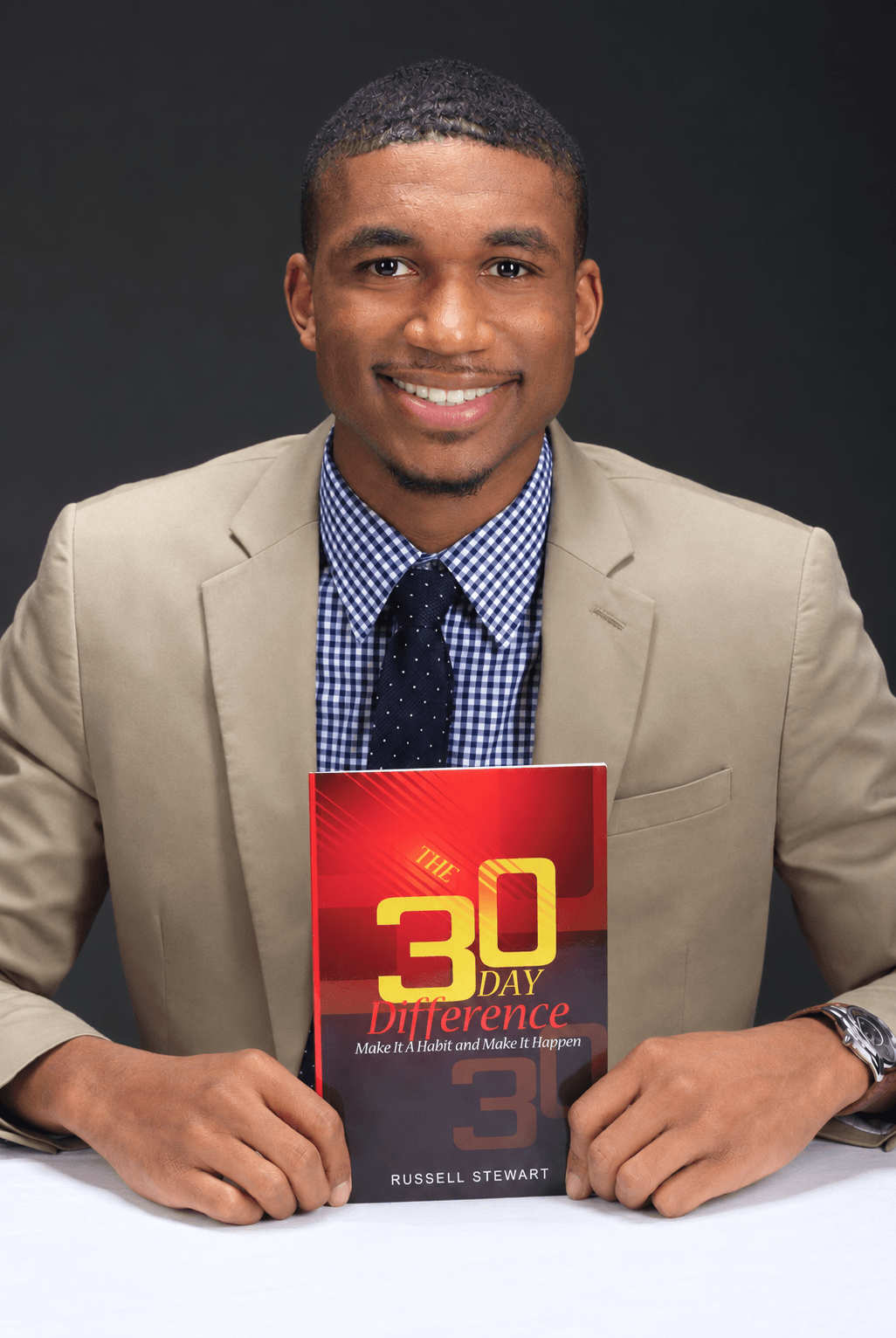 Young man in beige suit and blue shirt holding a book titled '30 Day Difference' smiling at camera.
