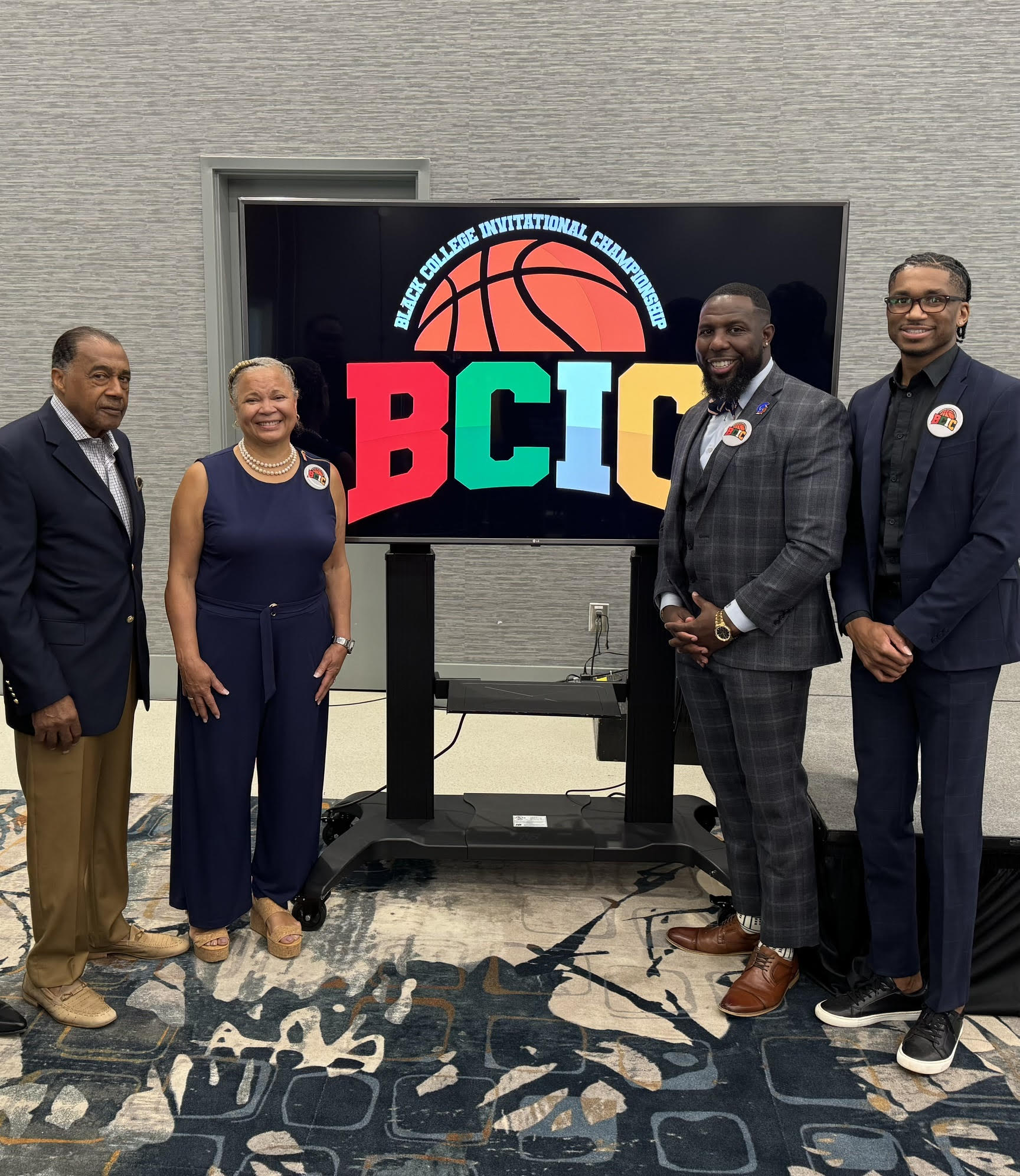 Five people stand in front of a screen displaying a basketball logo and the letters BCIC, smiling and dressed professionally.