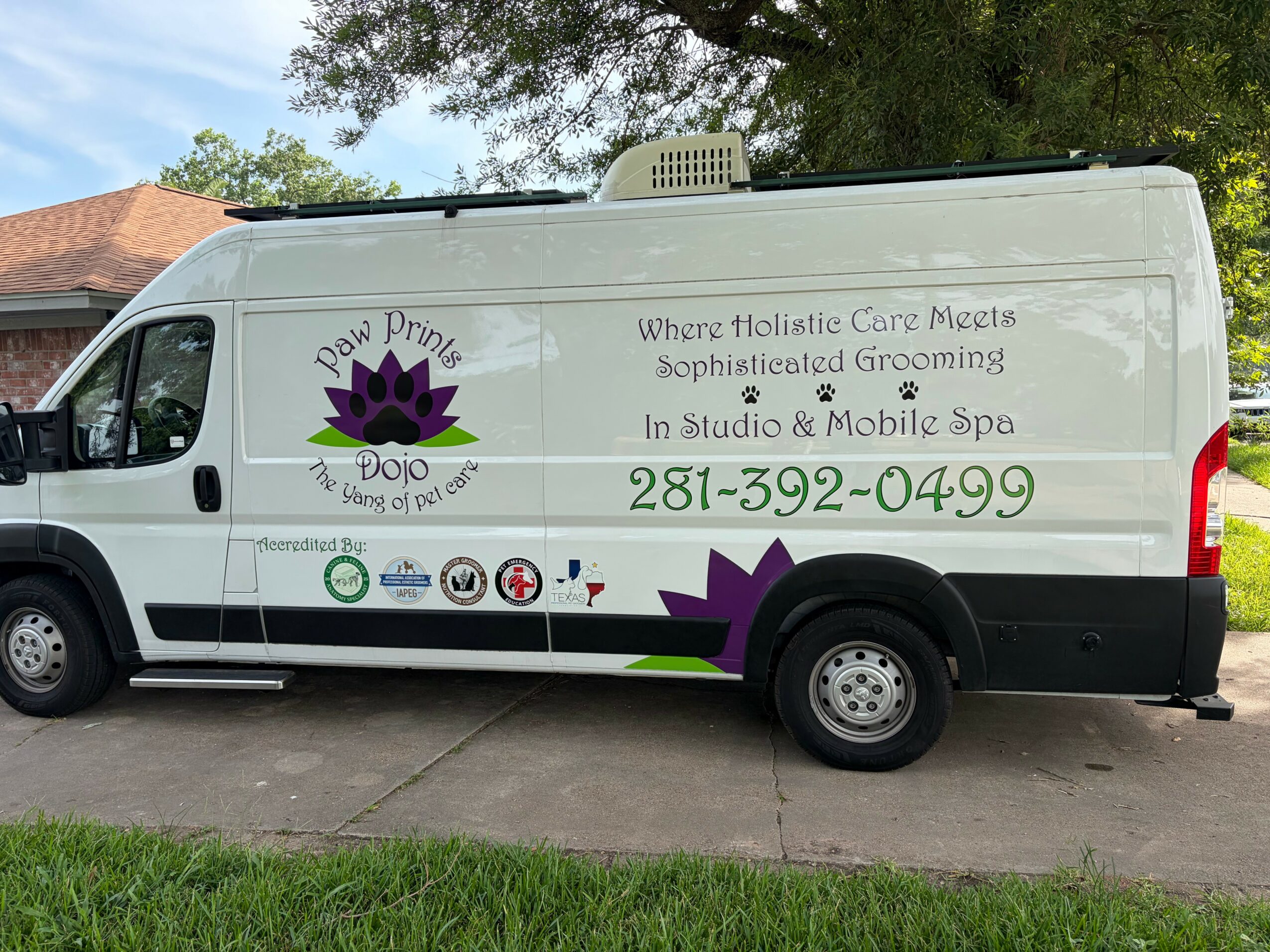 Side view of a white mobile spa van with purple lotus logo and text about holistic care, grooming, and contact number.
