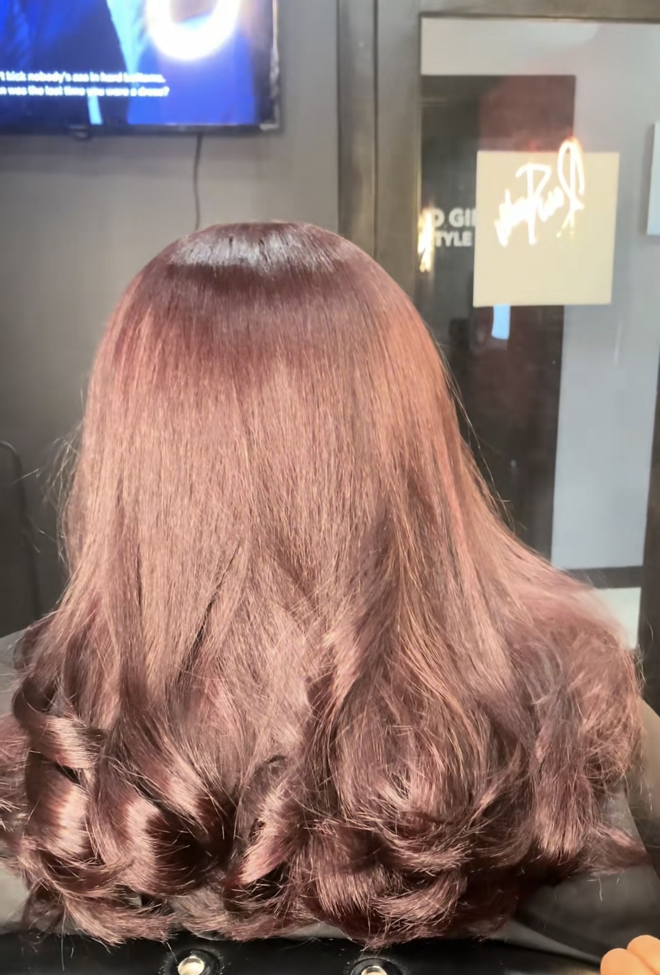 Back view of a person with long, wavy, reddish-brown hair in an indoor setting.