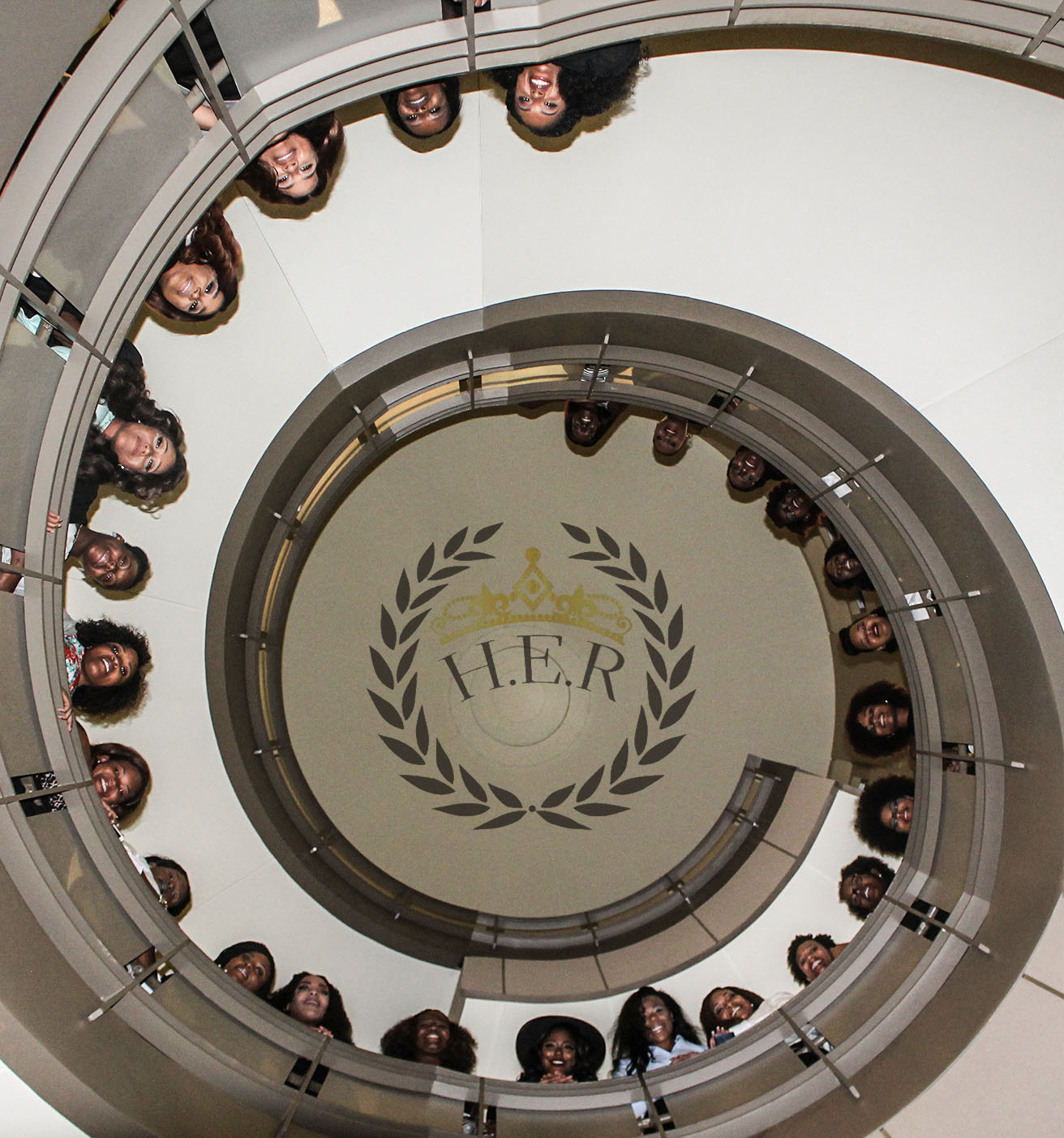 Group of people standing around a spiral staircase with a logo at the center, viewed from below.