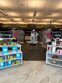 Interior of a store with shelves displaying various products, ceiling lights, and a carpeted area in the background.