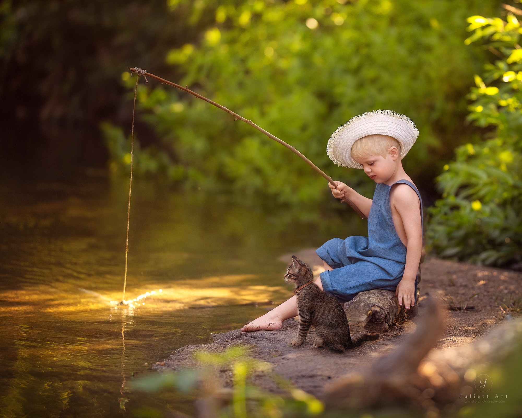 Child in a blue dress and large hat sitting on a rock by a river, fishing with a small dog nearby, surrounded by greenery.