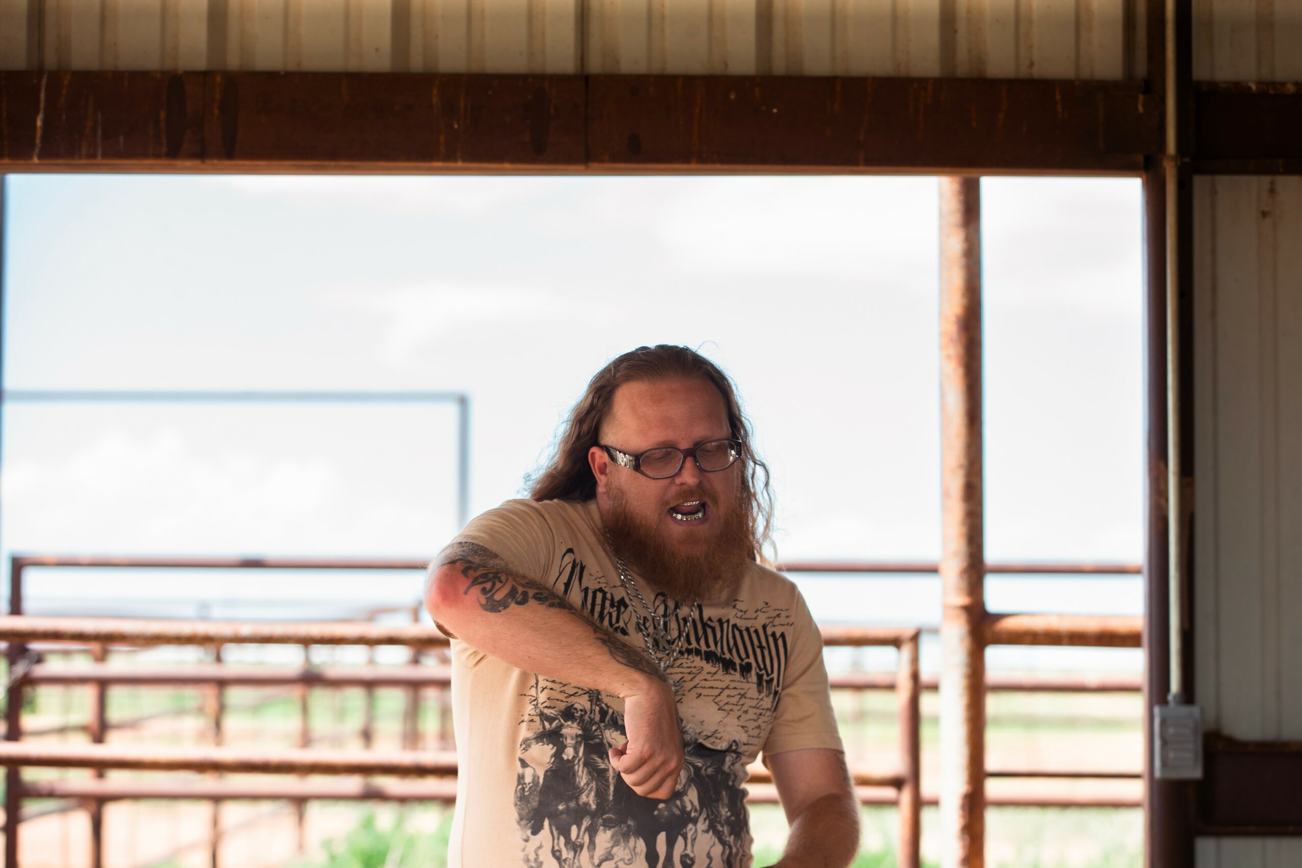 Man with glasses and long hair, smiling, inside a building with large window, outdoor scene visible behind.