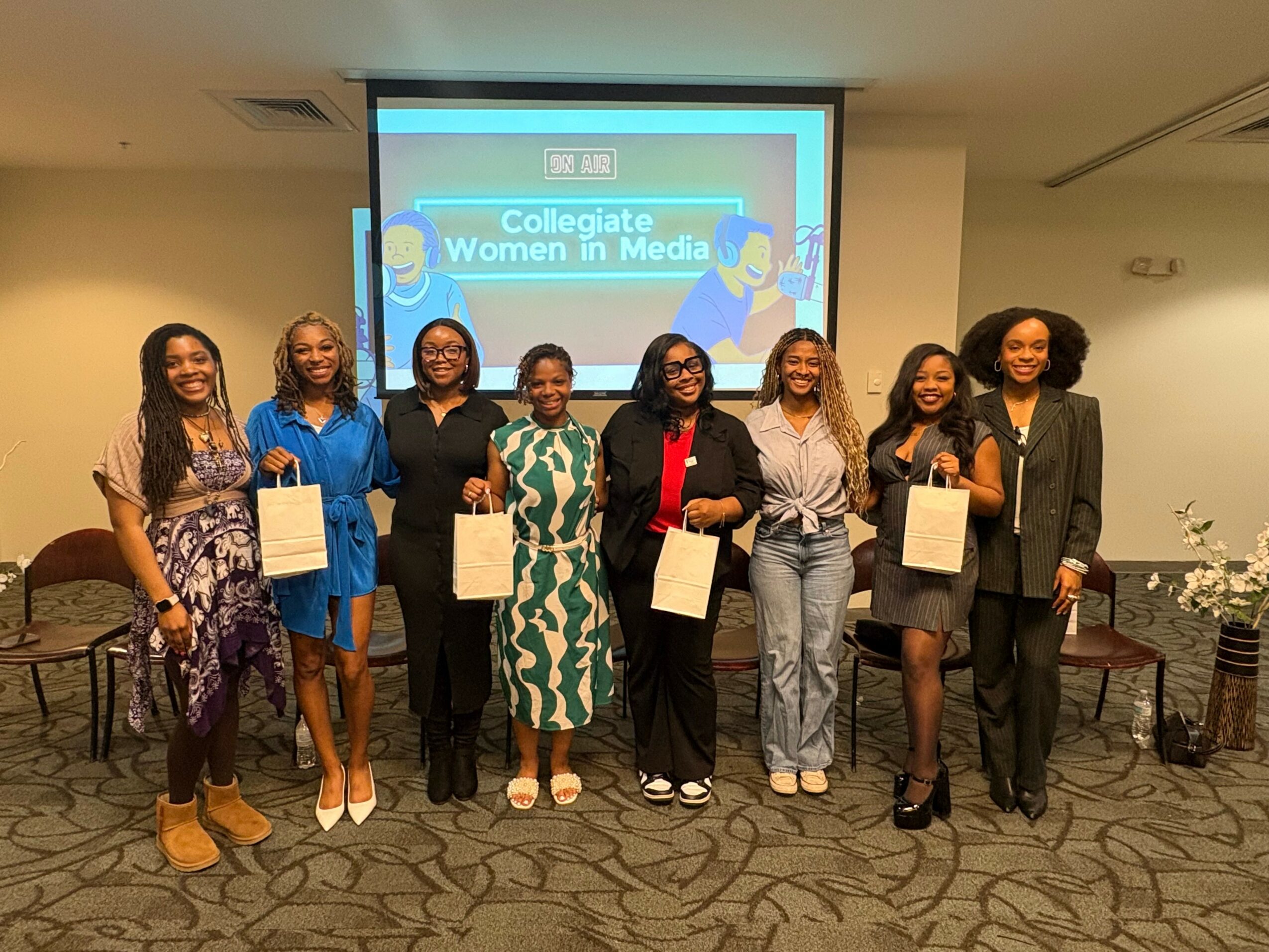 Group of eight women standing in front of a screen with a presentation slide, holding certificates, smiling.