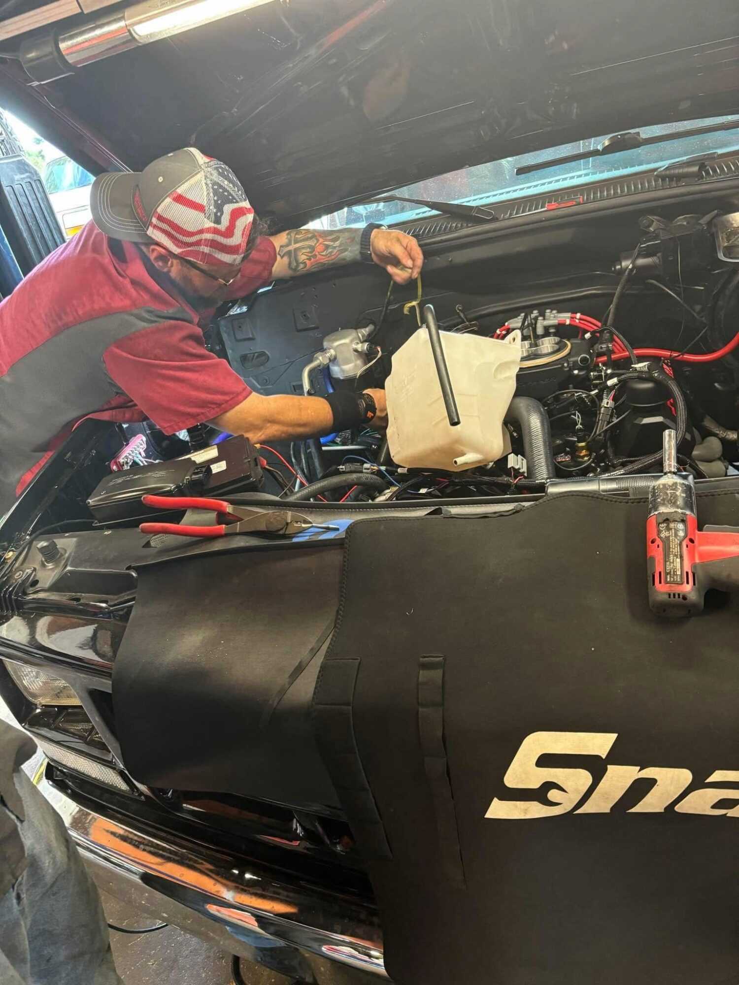 Person wearing a red shirt and striped hat working on a car engine with tools and equipment around.