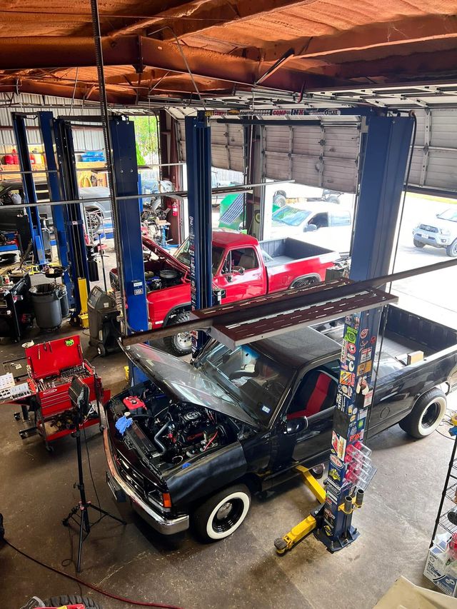 View of a garage with two trucks, one black and one red, surrounded by tools and equipment, seen from above.