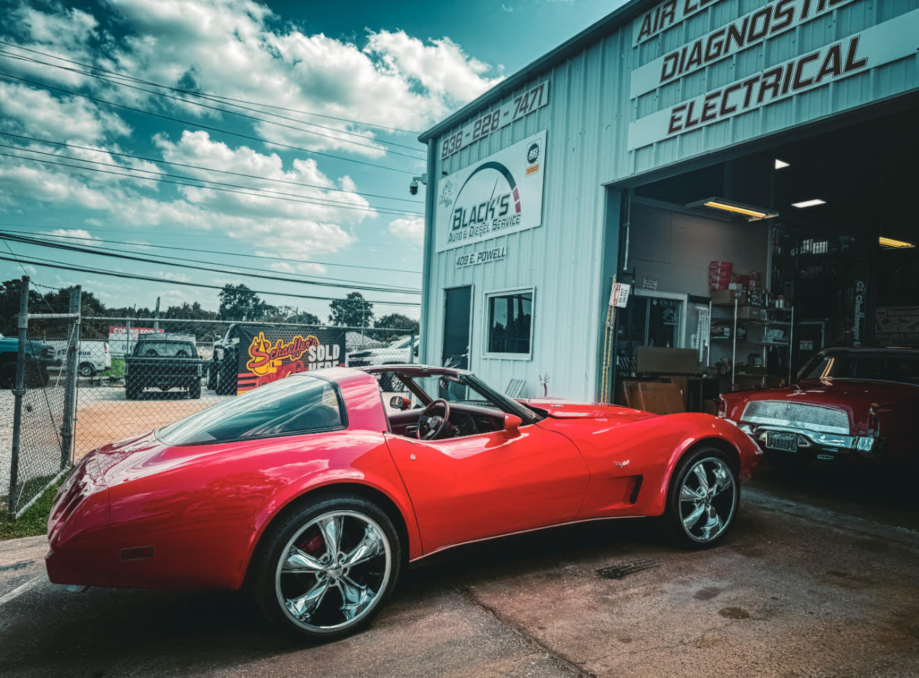 Red sports car parked outside an automotive repair shop with a sign reading 'Electrical' and 'Diagnostics'.