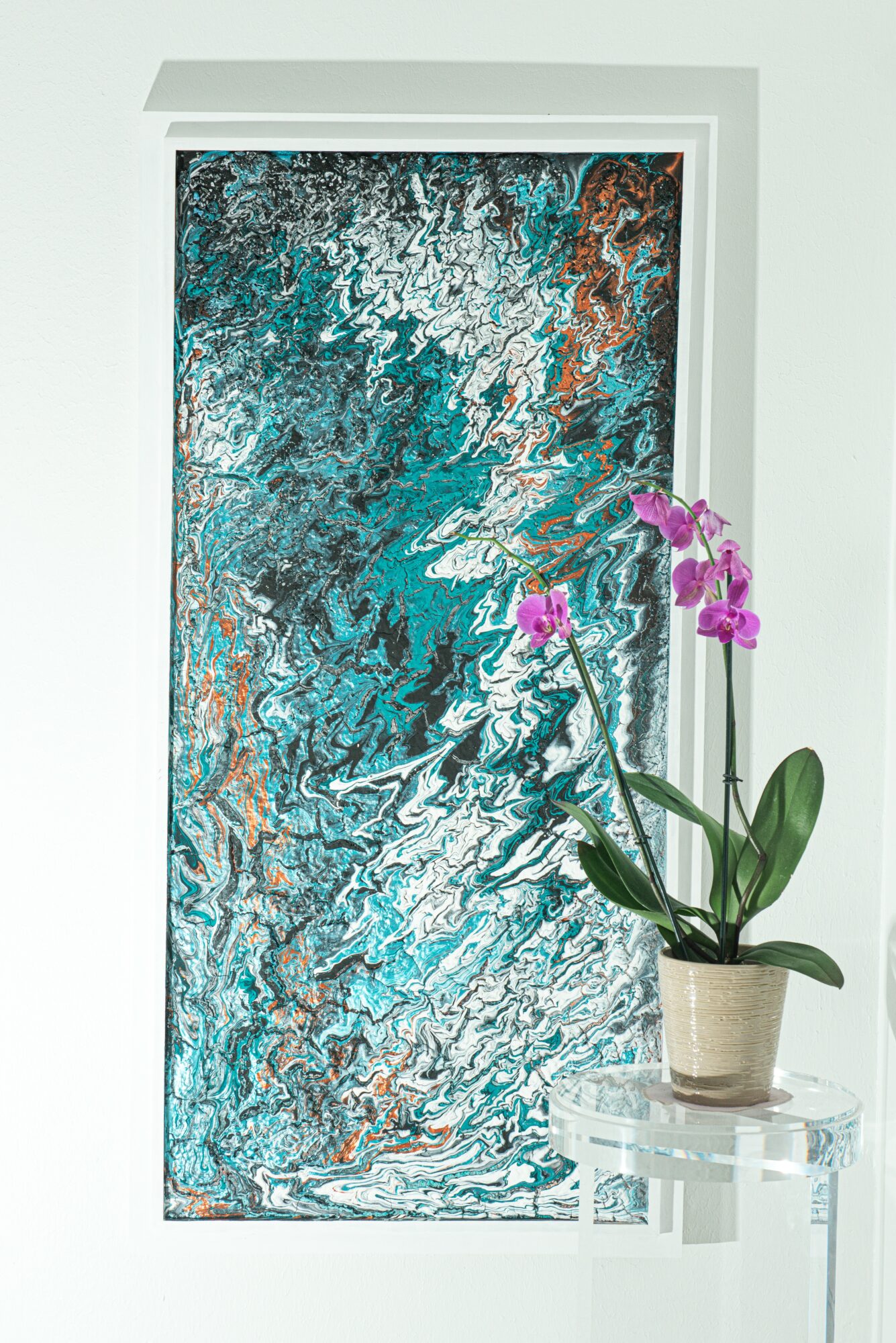 Abstract artwork with blue, white, and copper colors, next to a potted purple orchid on a clear stand