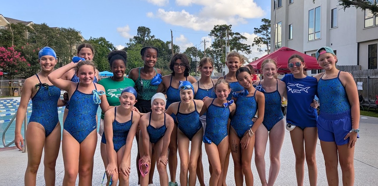Group of young girls in blue swimsuits standing outdoors near a pool, smiling and posing for a photo.