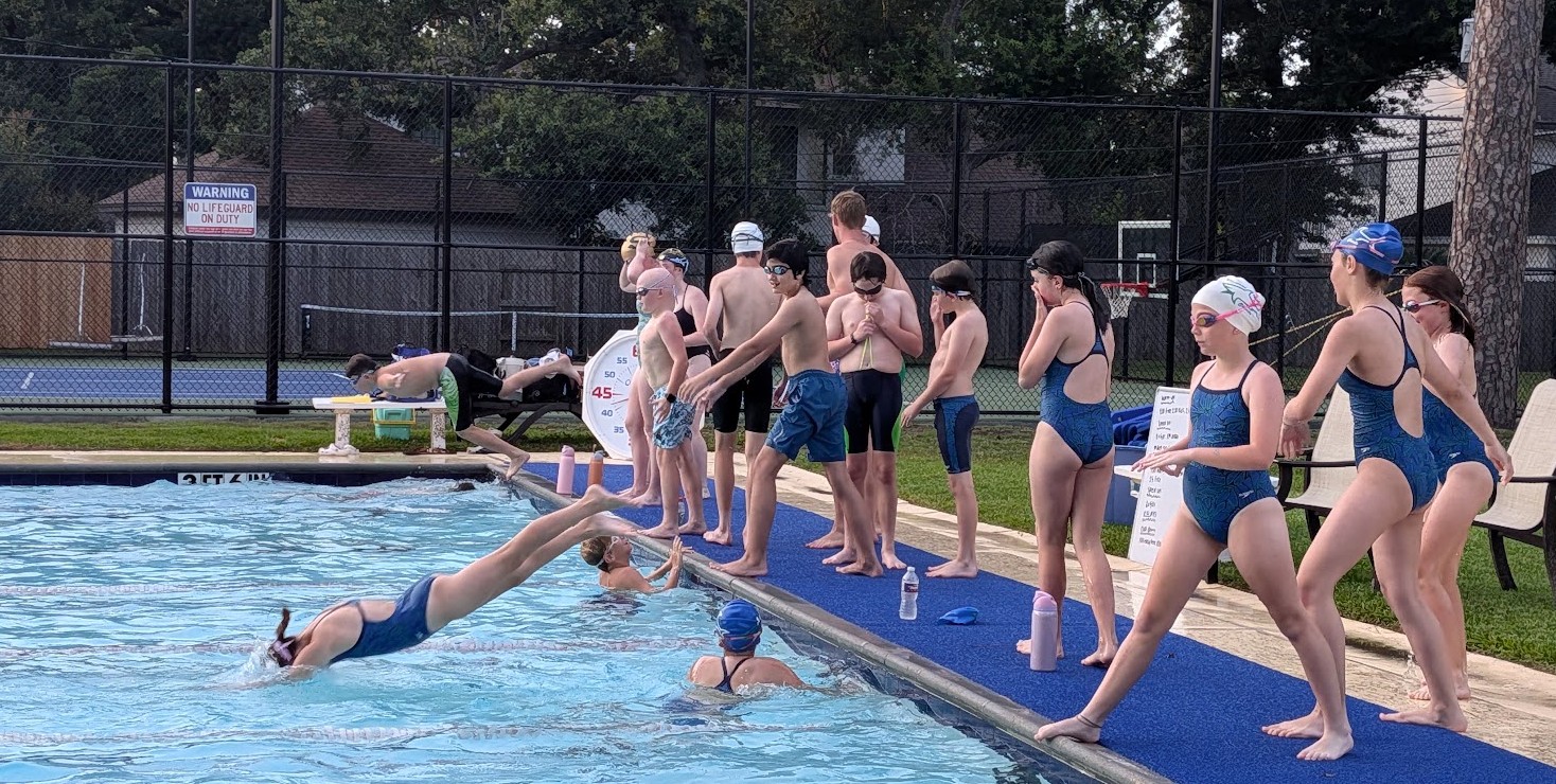 Children and adults line up on poolside, preparing to jump into the water, with some already swimming.