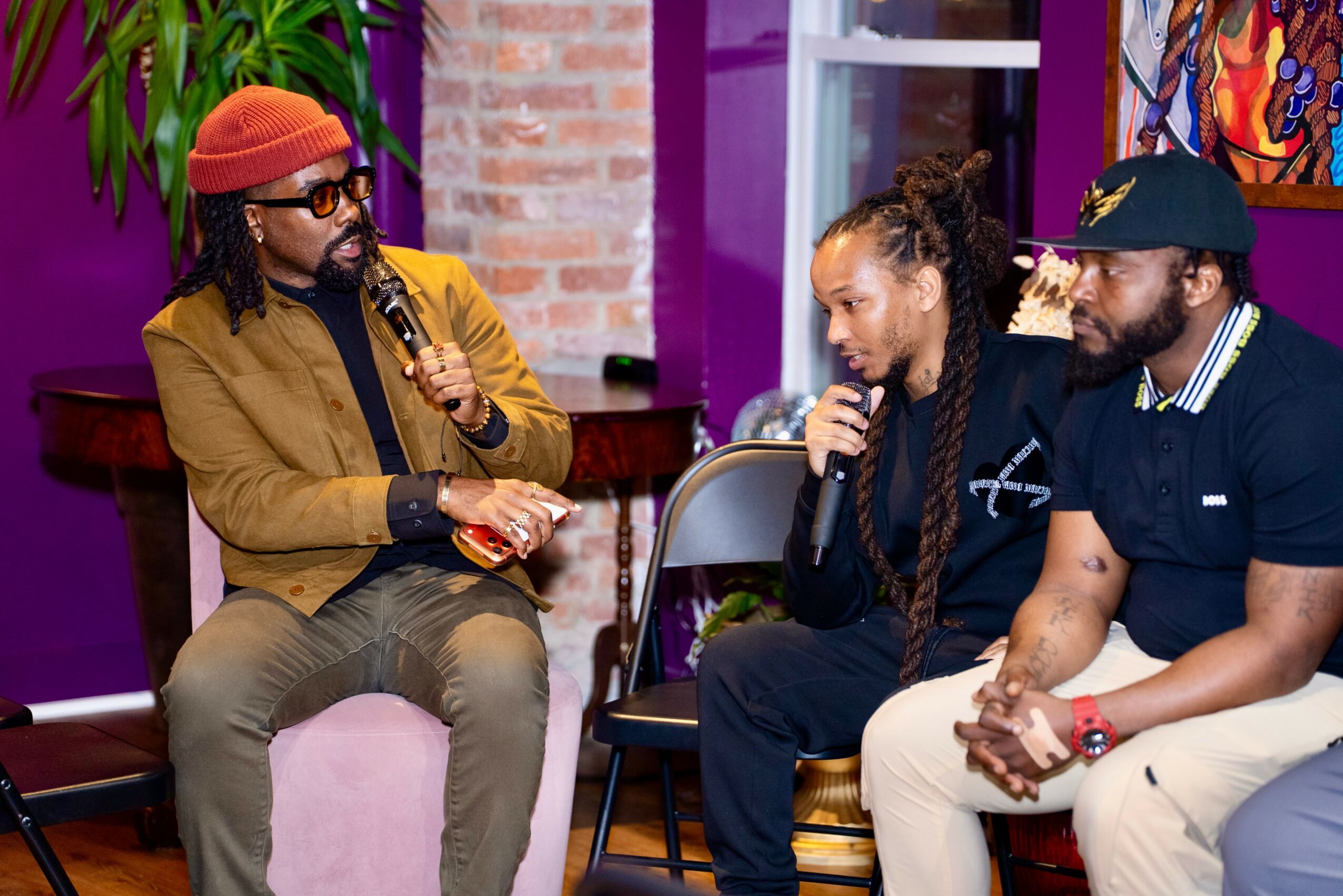 Three people sitting and talking indoors, two women and one man, with colorful background and purple walls.