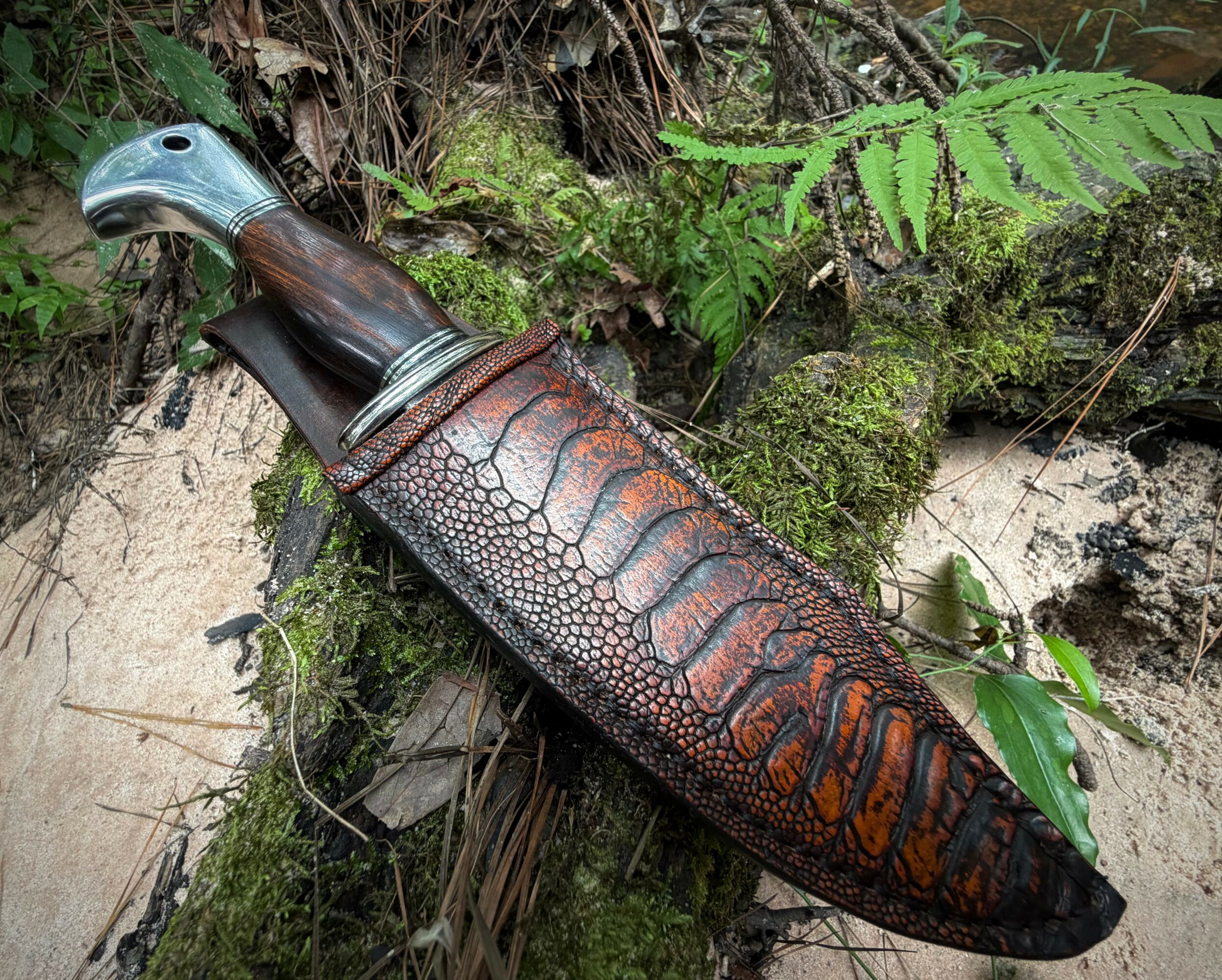 A carved wooden object resembling a bird's head and a long, textured body, lying on mossy ground with green plants.