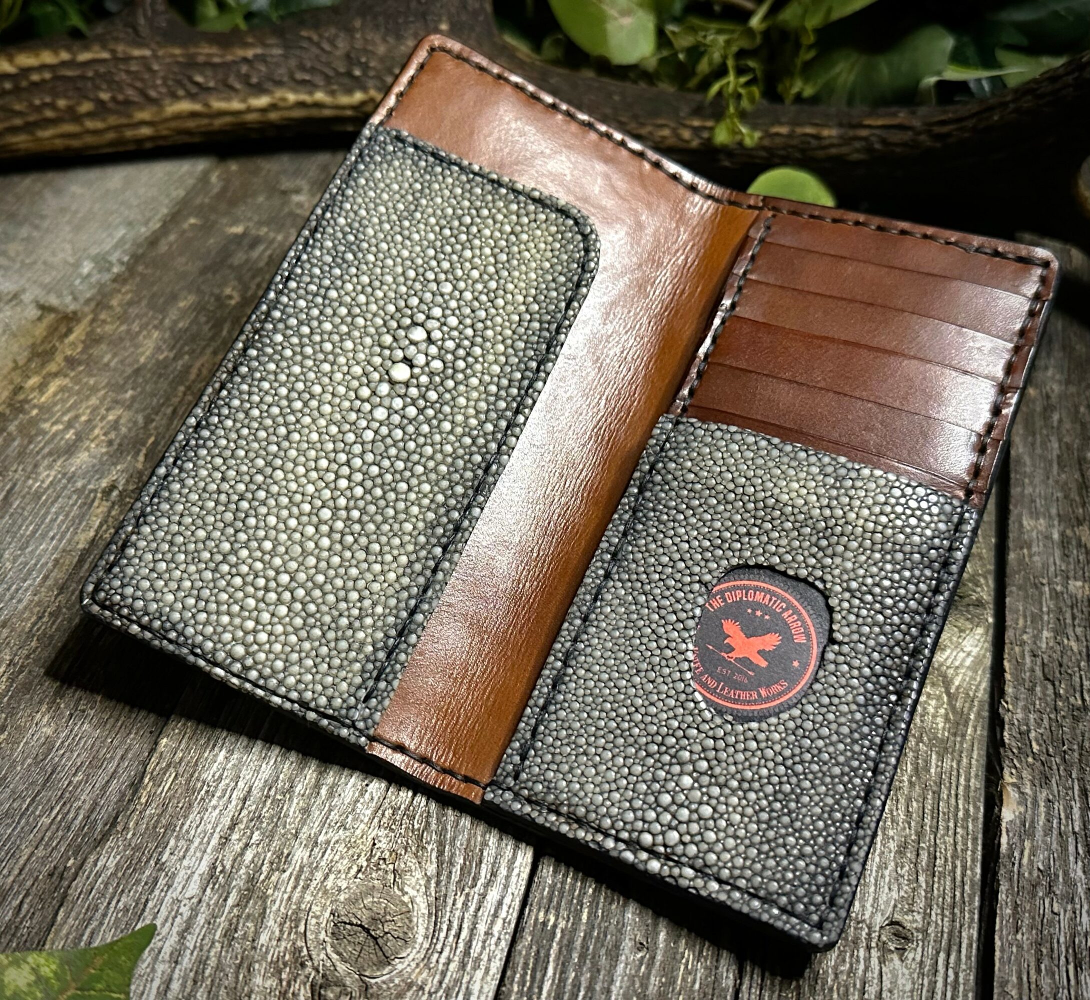 Open wallet with card slots and textured pockets on a wooden surface, with green plants nearby.