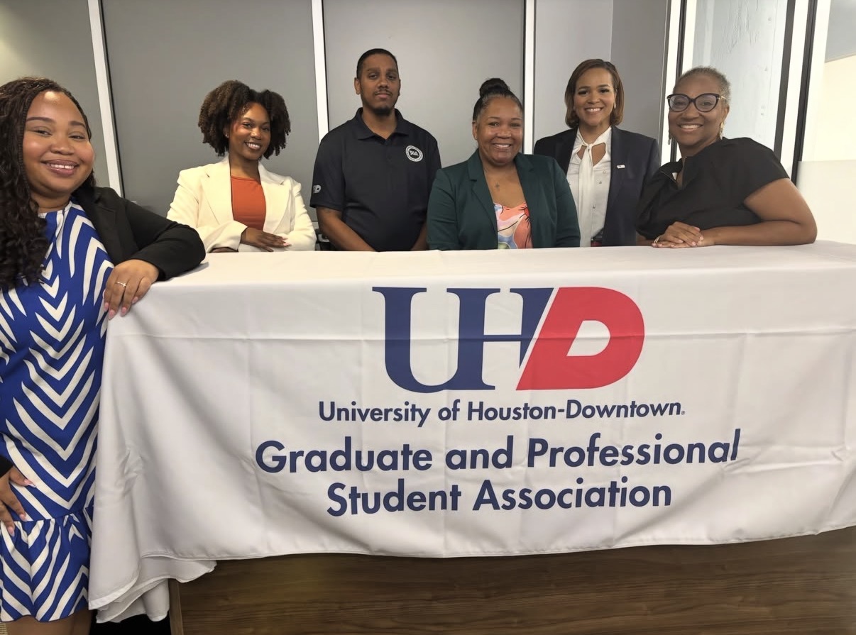 Six people standing behind a table with a banner reading 'University of Houston-Downtown Graduate and Professional Student Association.'