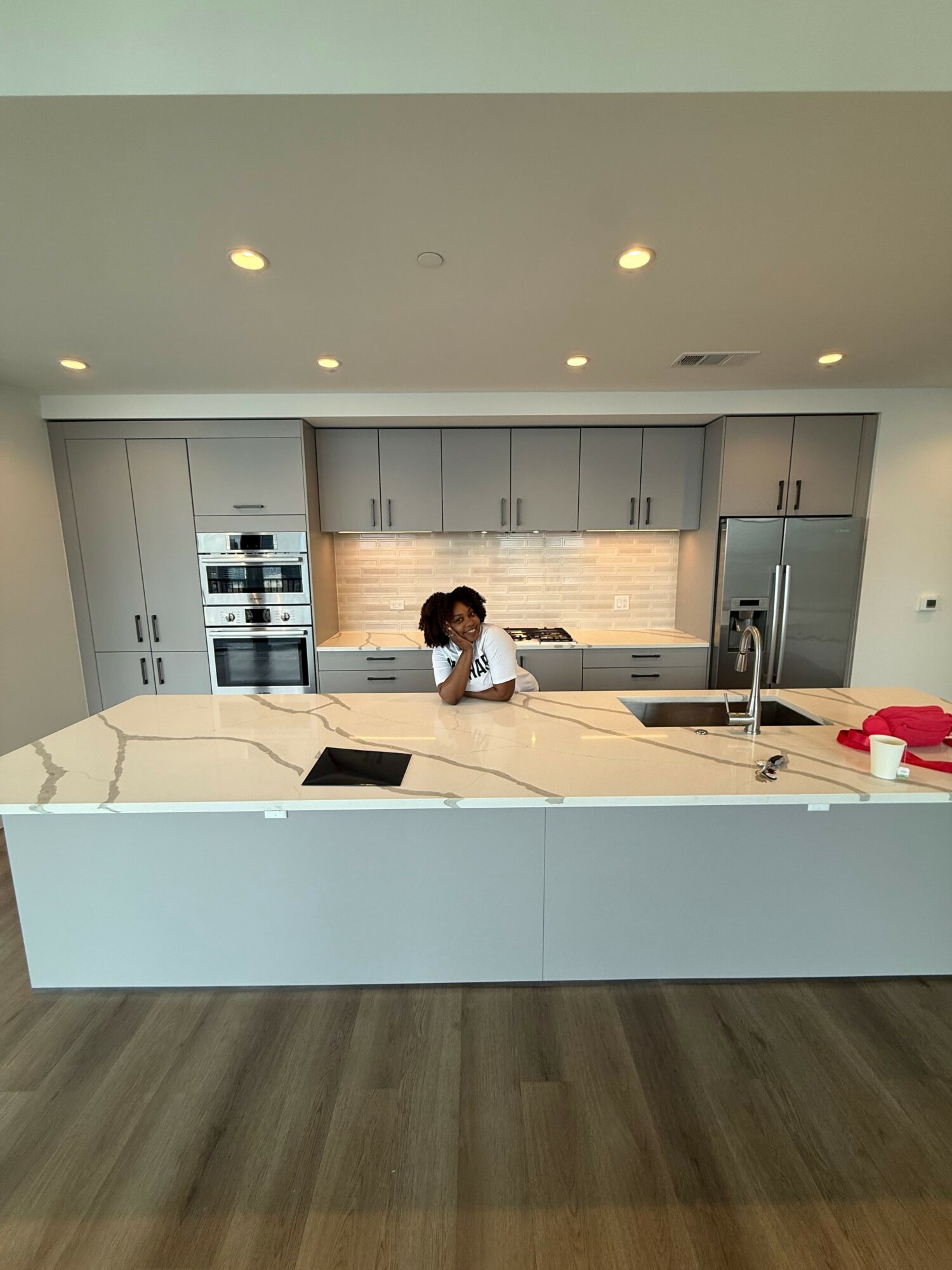 Person sitting at kitchen counter with gray cabinets, stainless steel appliances, and a white backsplash.