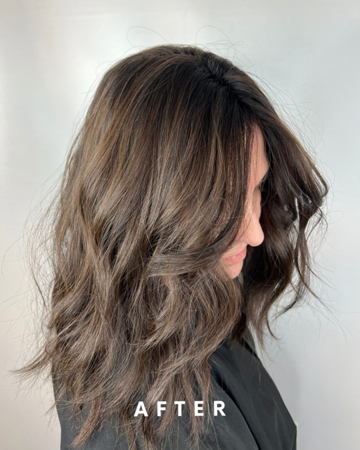 Side view of a woman with wavy, shoulder-length hair, looking down, with a neutral background.