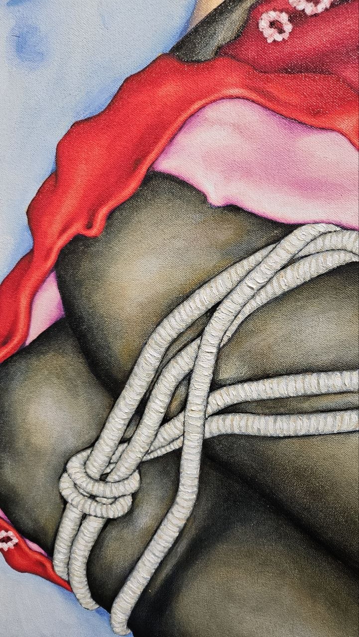 Close-up of a person wearing a red and pink garment with gray ropes around their waist, dark skin visible.