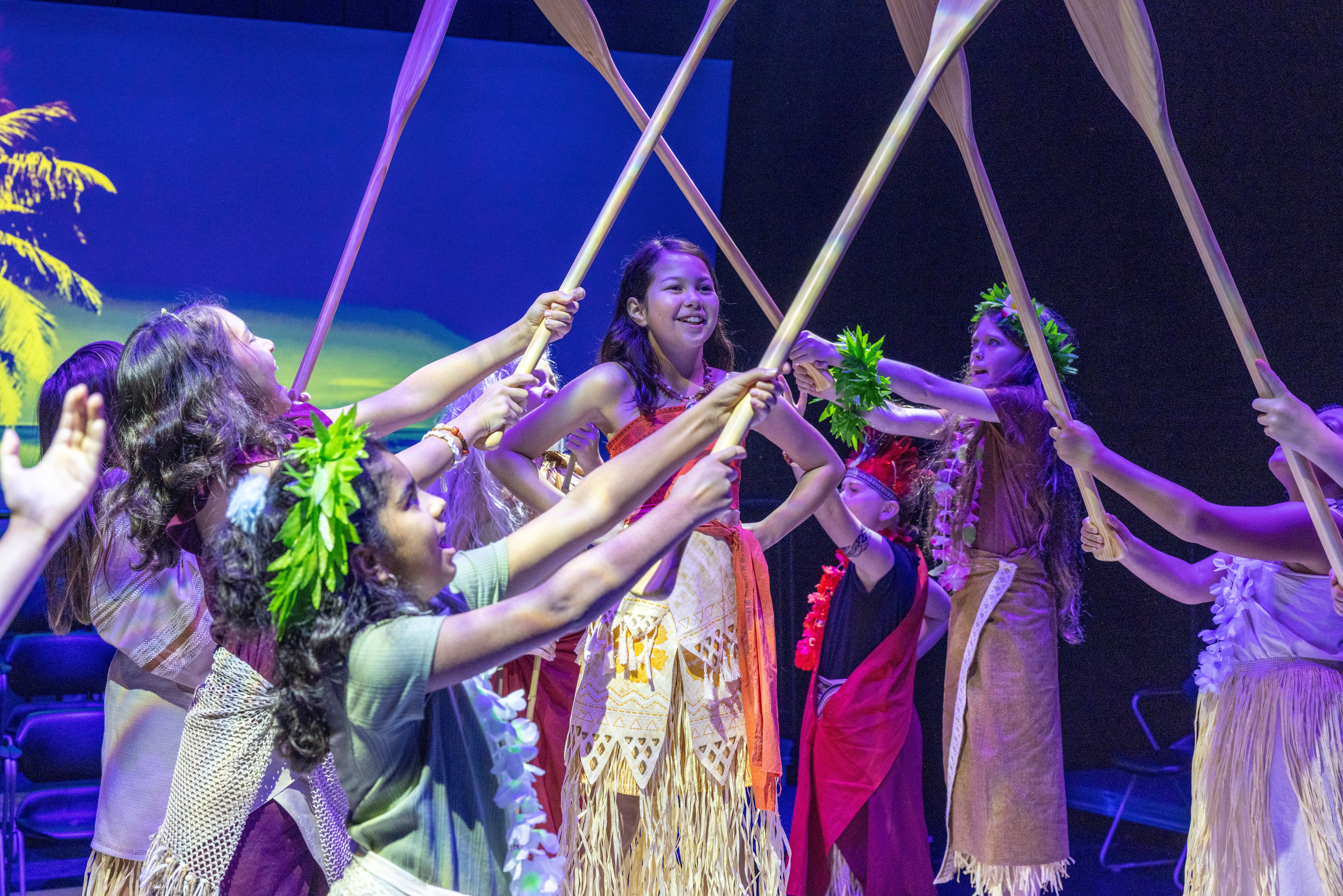 Group of women in traditional costumes holding flags and smiling during a performance, stage background visible.