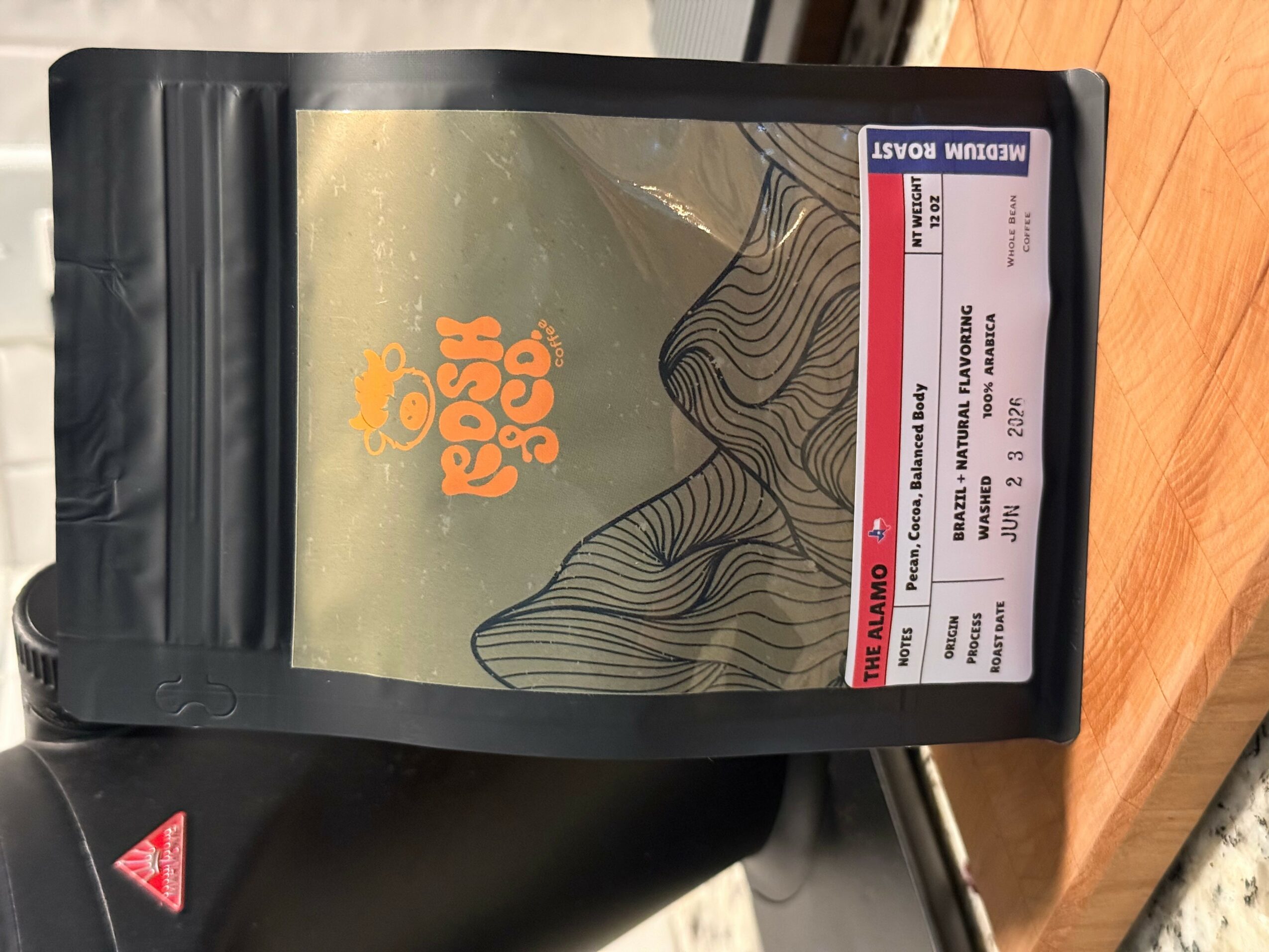 A black package with a yellow label and orange logo, placed on a wooden surface, with a red and white label on top.