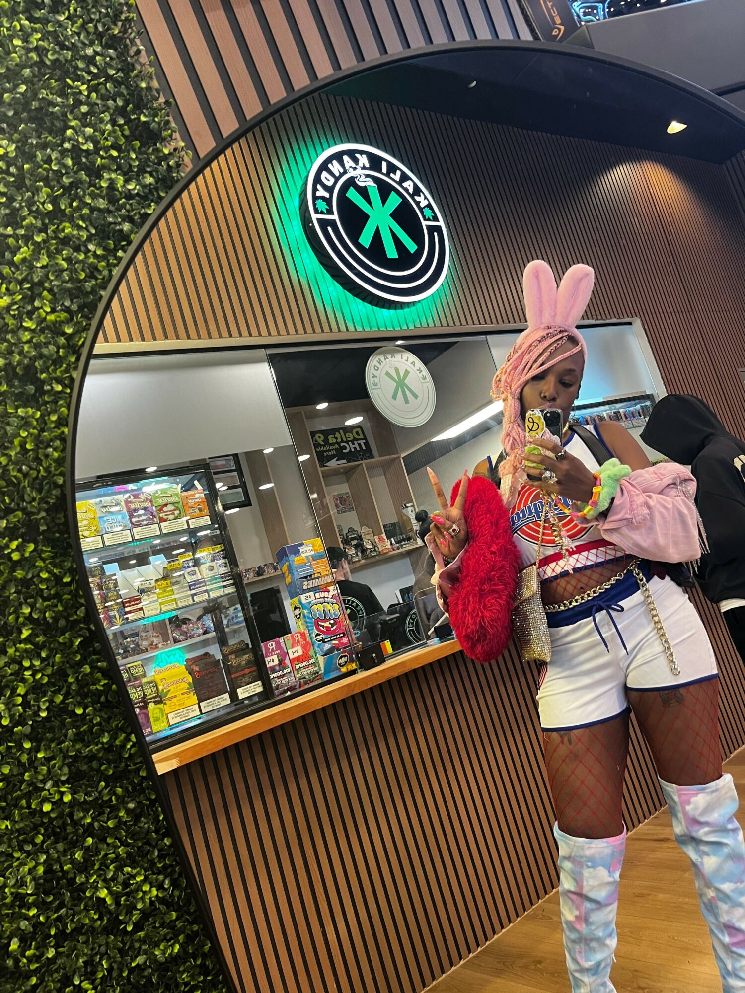 Person dressed in colorful clothing with a pink bunny hat, standing in front of a store display, holding a bag.