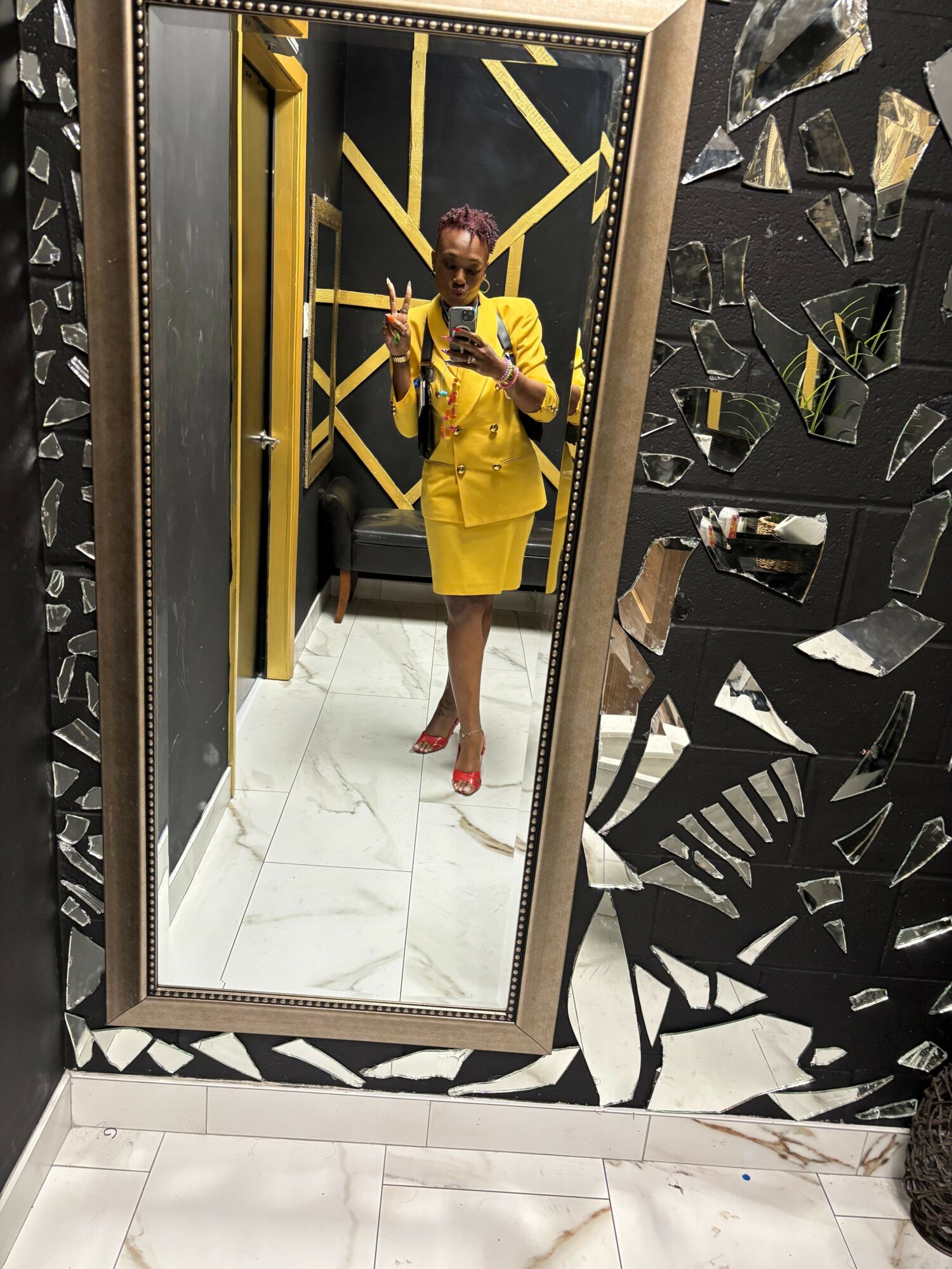 Person in yellow dress taking a mirror selfie in a stylish room with black and gold decor.