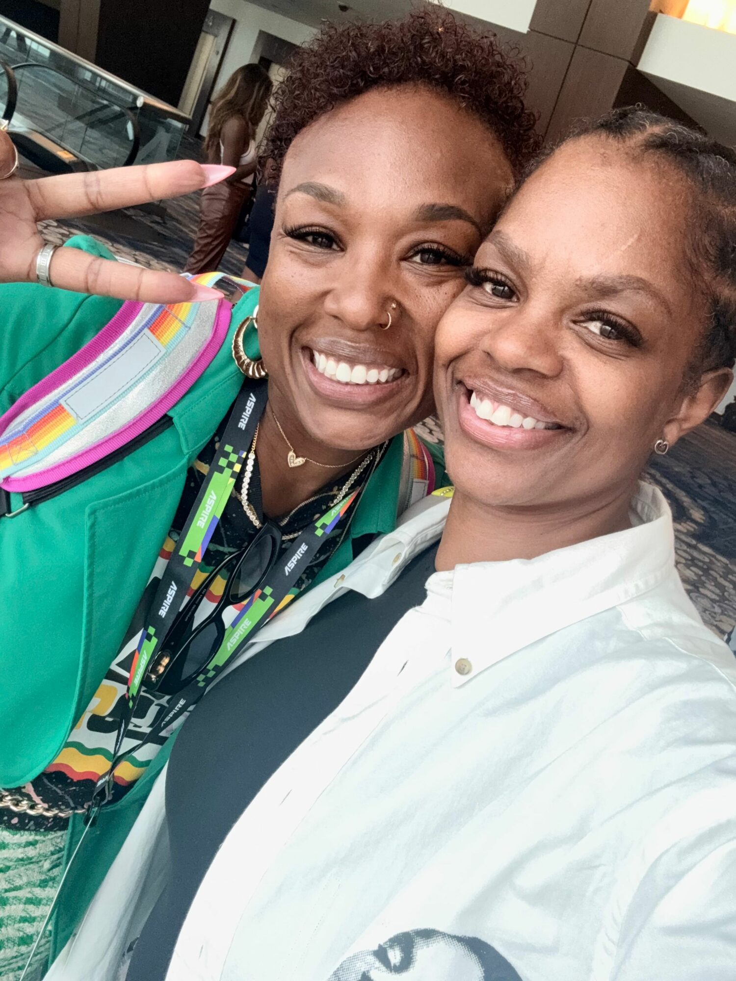 Two women smiling, one making a peace sign, in a close-up selfie.