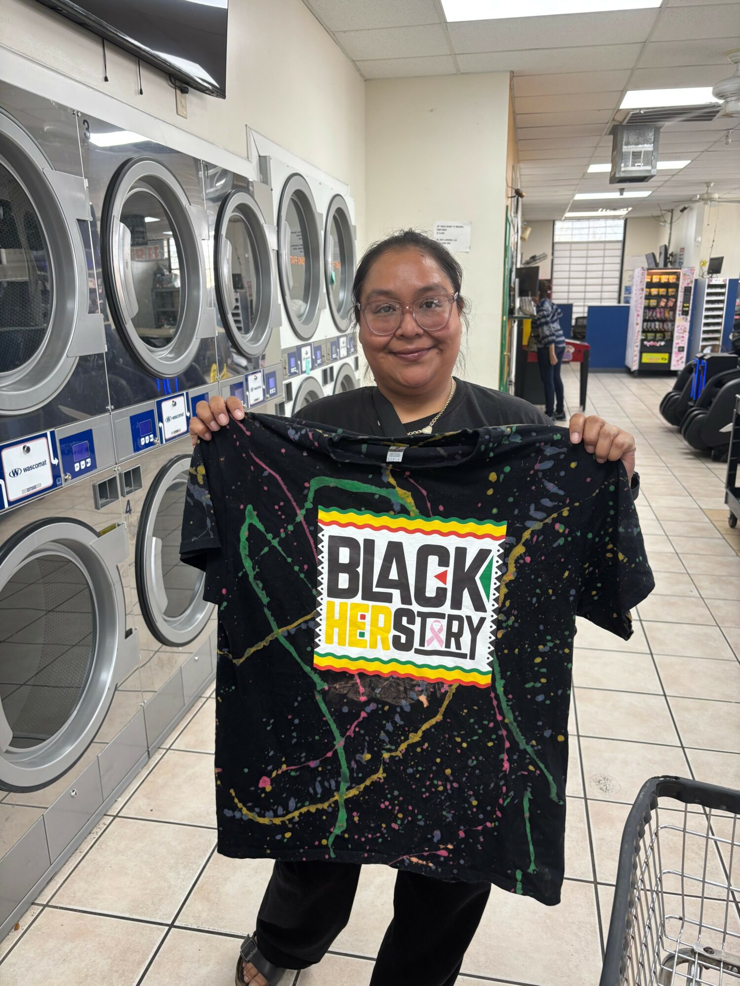 Person holding a Black Lives Matter T-shirt in a laundromat with washing machines in the background.