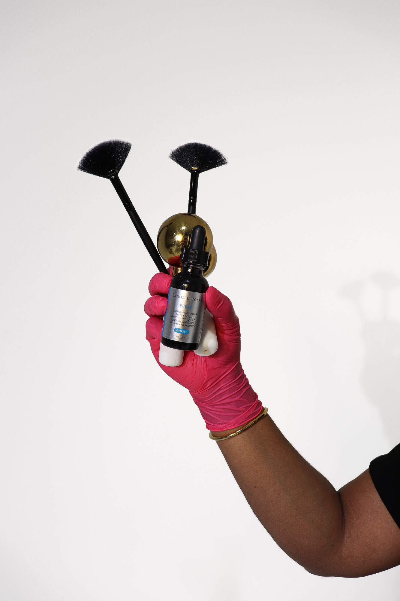 A hand wearing a pink glove holds a small metallic object with two black brushes attached, against a plain white background.