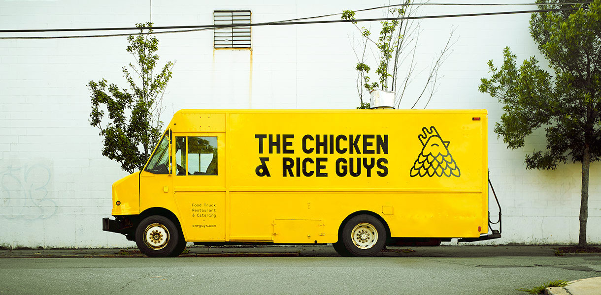 Yellow food truck with black text and a chicken illustration, parked on street with trees and power lines