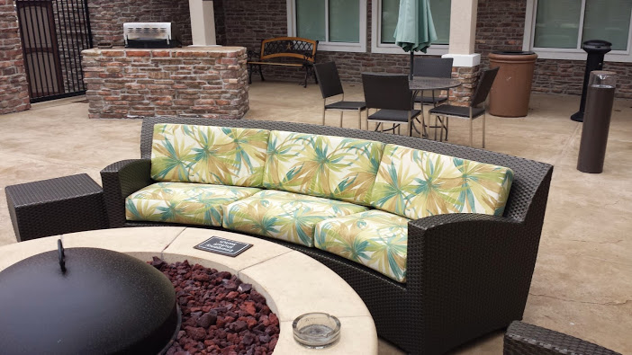 Outdoor seating area with a black wicker sofa with a floral cushion, a round table, and chairs in the background.