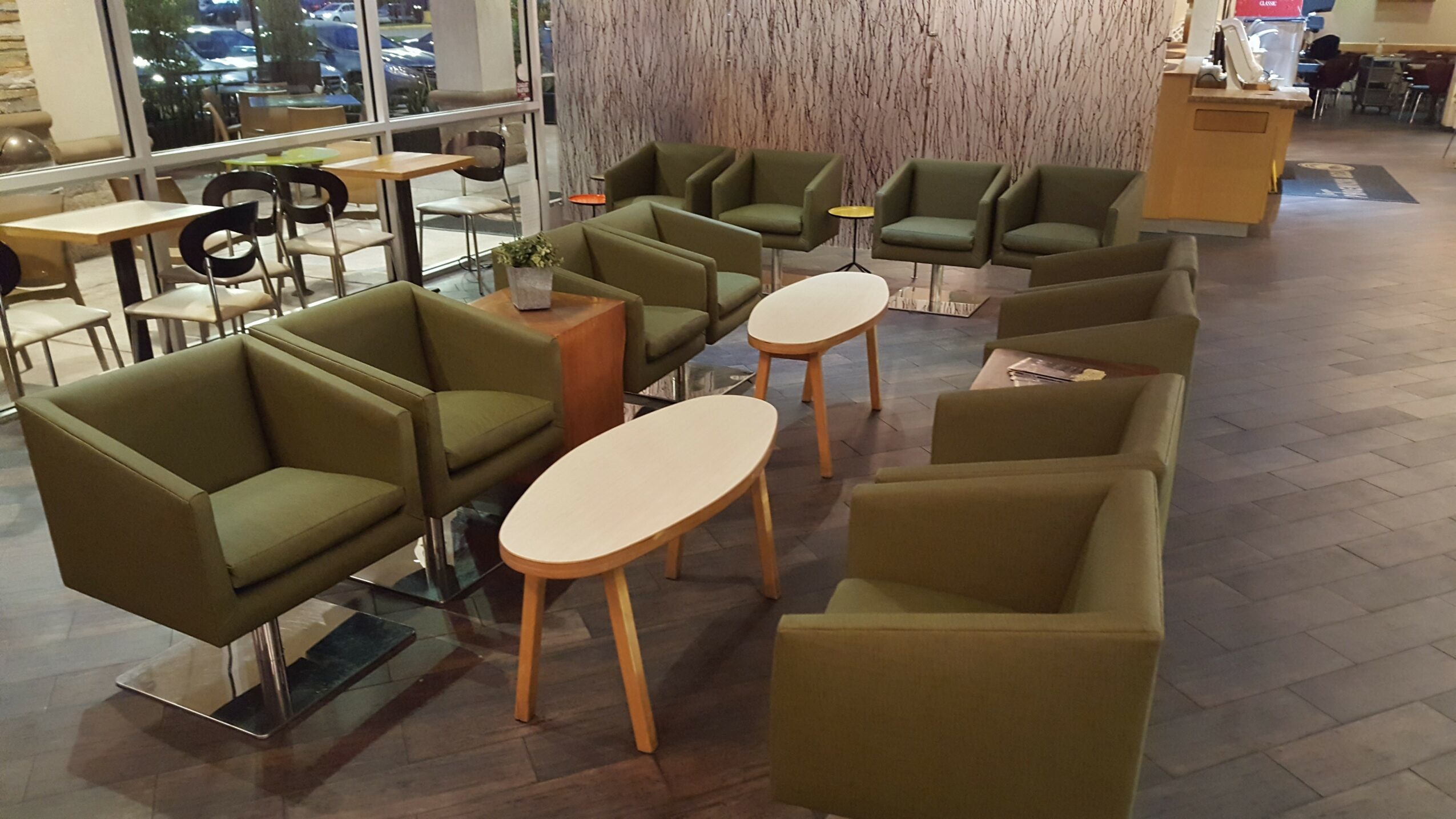 Seating area with green armchairs and oval tables in a lounge or cafe setting.