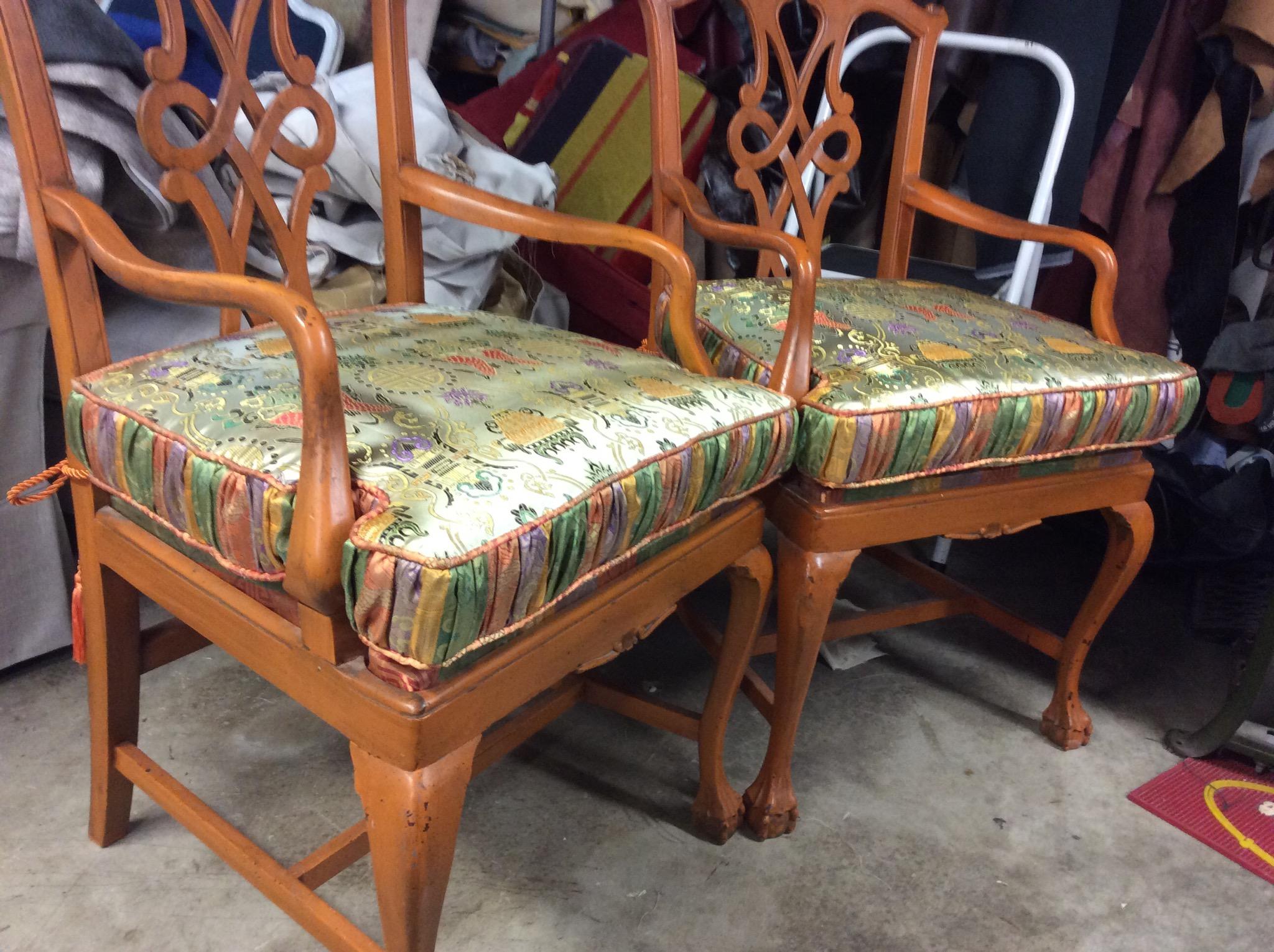 Two wooden chairs with floral cushions and ornate backrests, placed side by side in a room with various items around.