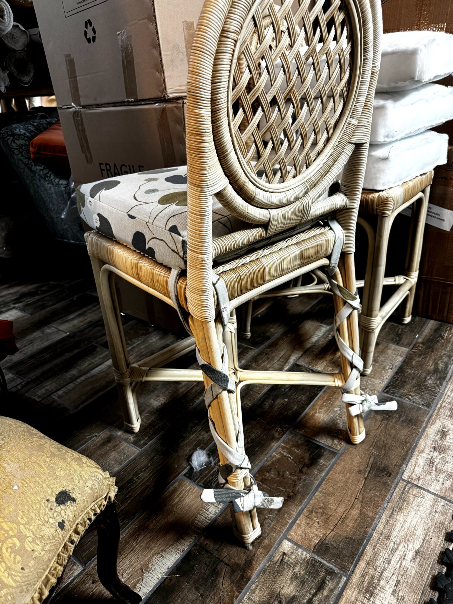 Stacked rattan chairs with woven circular backs and patterned cushions on a wooden floor.