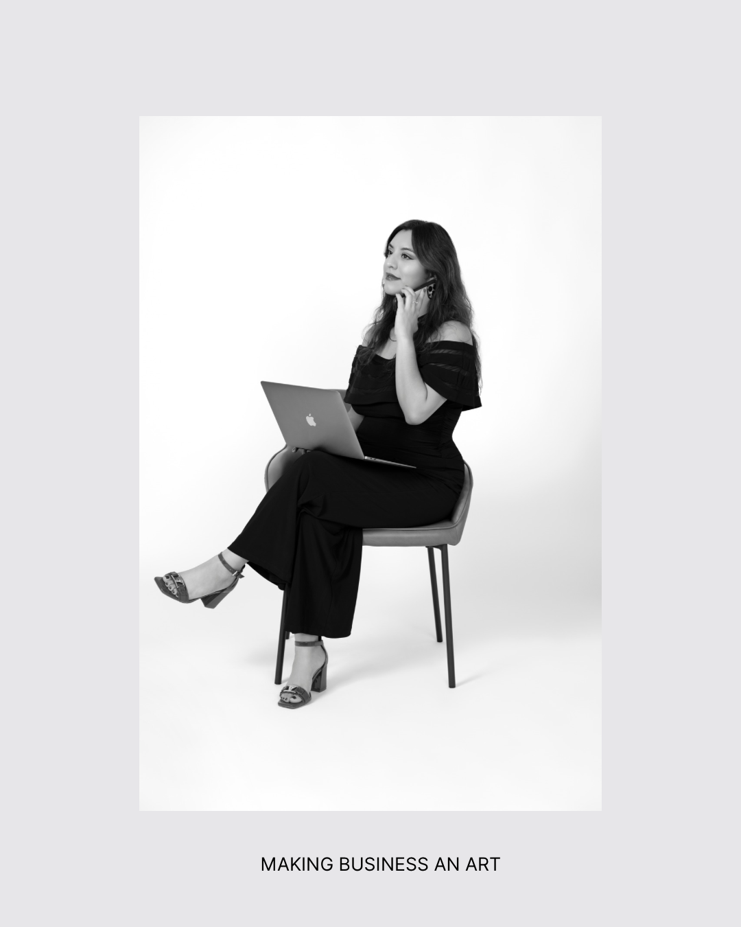 Woman sitting on a chair with a laptop, smiling and looking to the side, against a plain background.