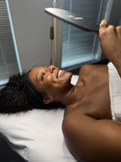 Person lying on a bed, smiling, holding a large knife above their face, with a towel covering their lower body.
