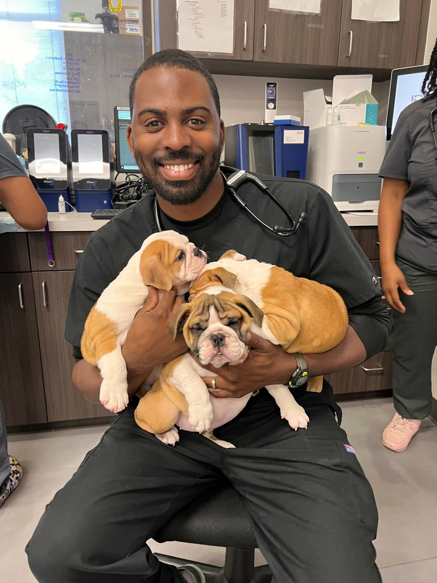 Person holding a puppy with a person sitting nearby in a room with medical equipment