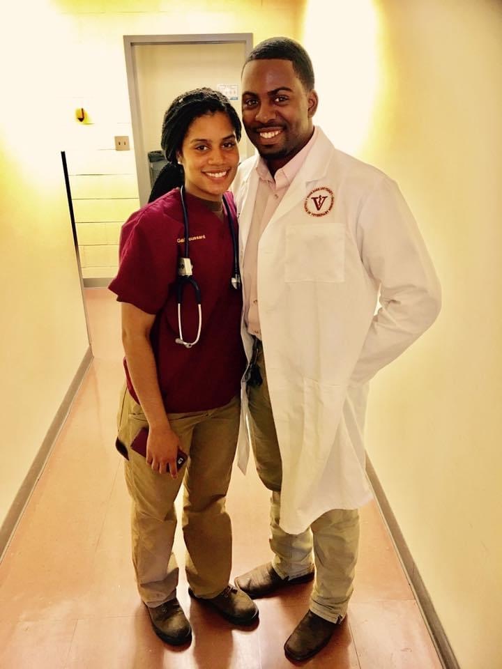 A young girl and a man in a white coat stand together in a hallway, smiling at the camera.