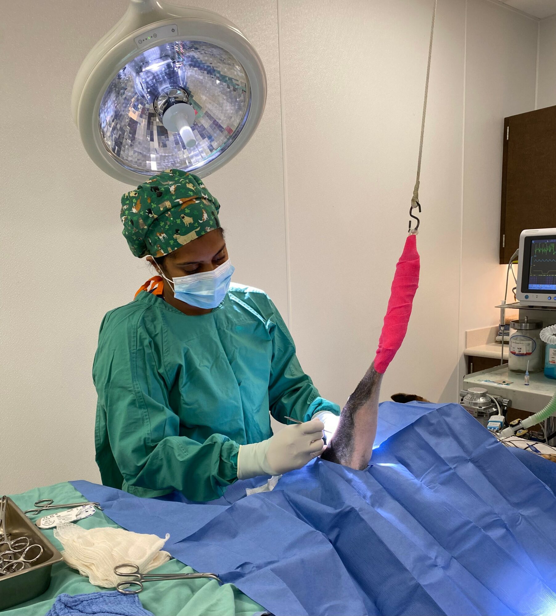 Medical professional in surgical gown and mask prepares a patient’s leg in an operating room.