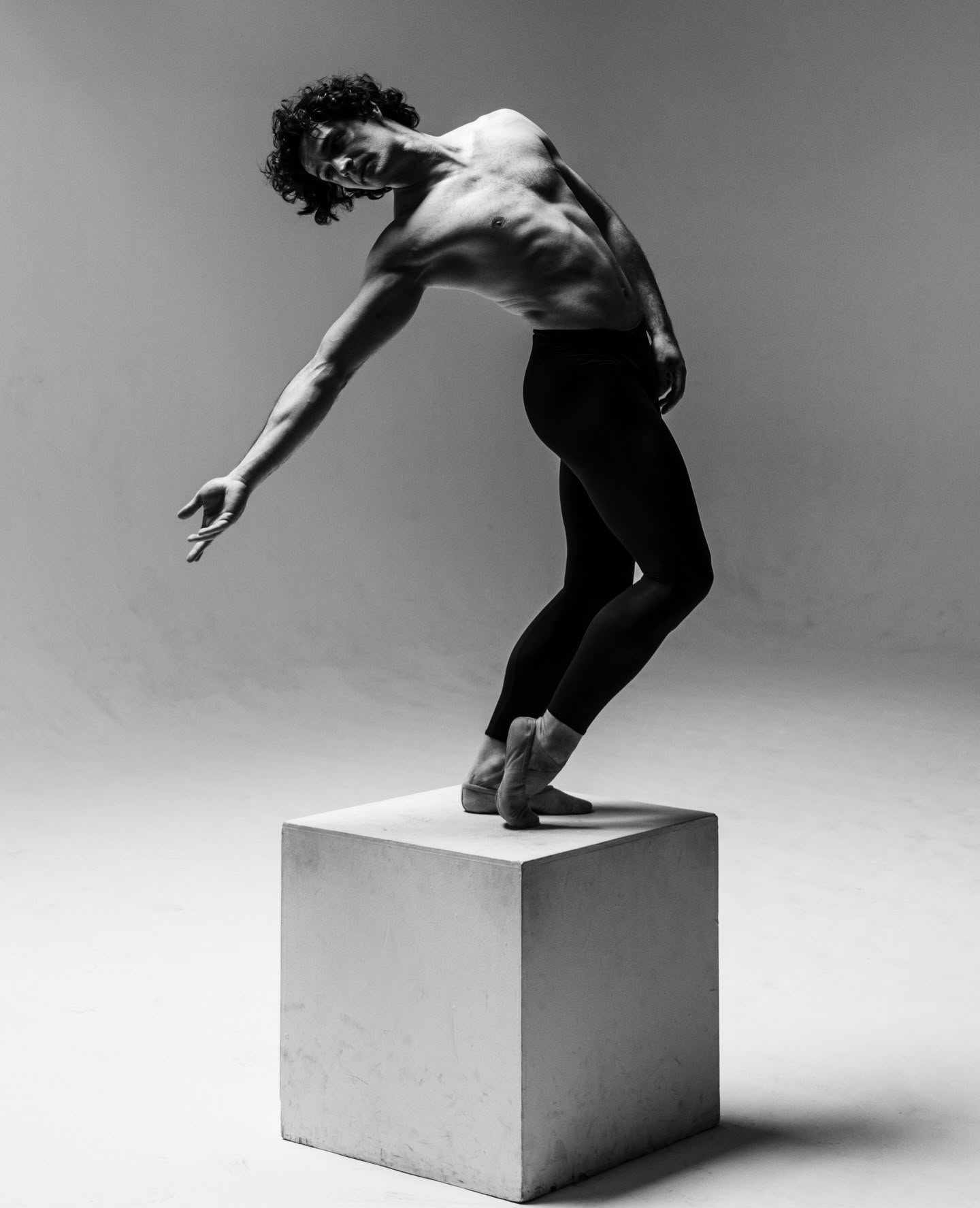 Person balancing on a cube with arms extended and body arched backward, in black and white.
