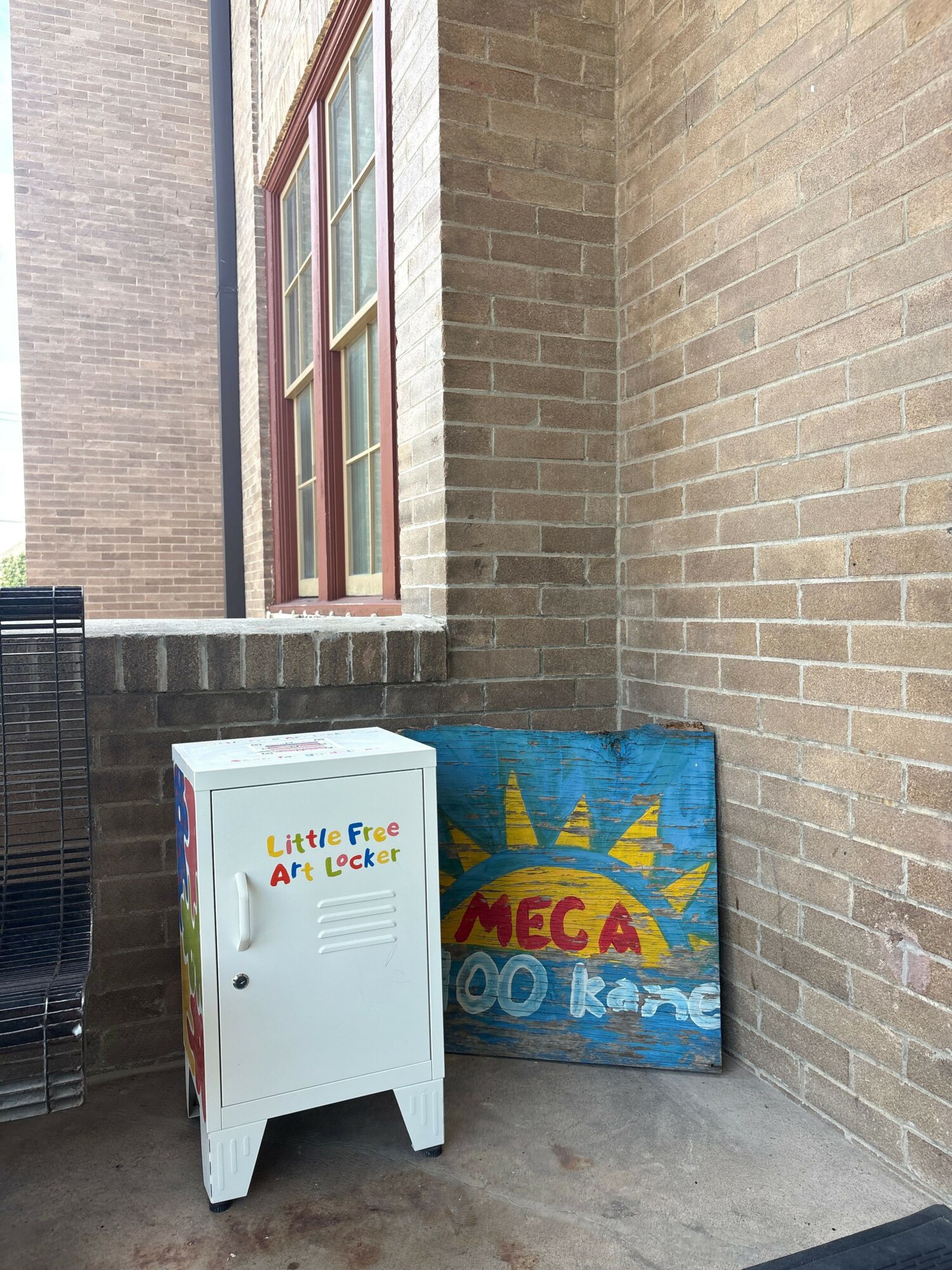 Brick wall and window with a vending machine and a colorful sign outside.